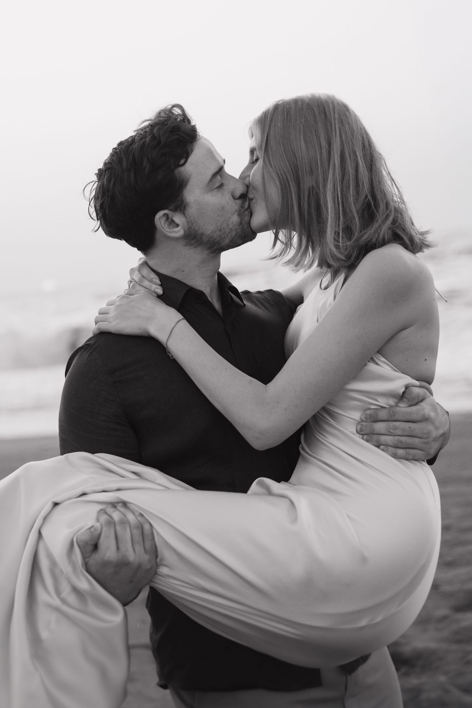 A romantic black and white photo series showing a couple embracing and kissing on the beach.