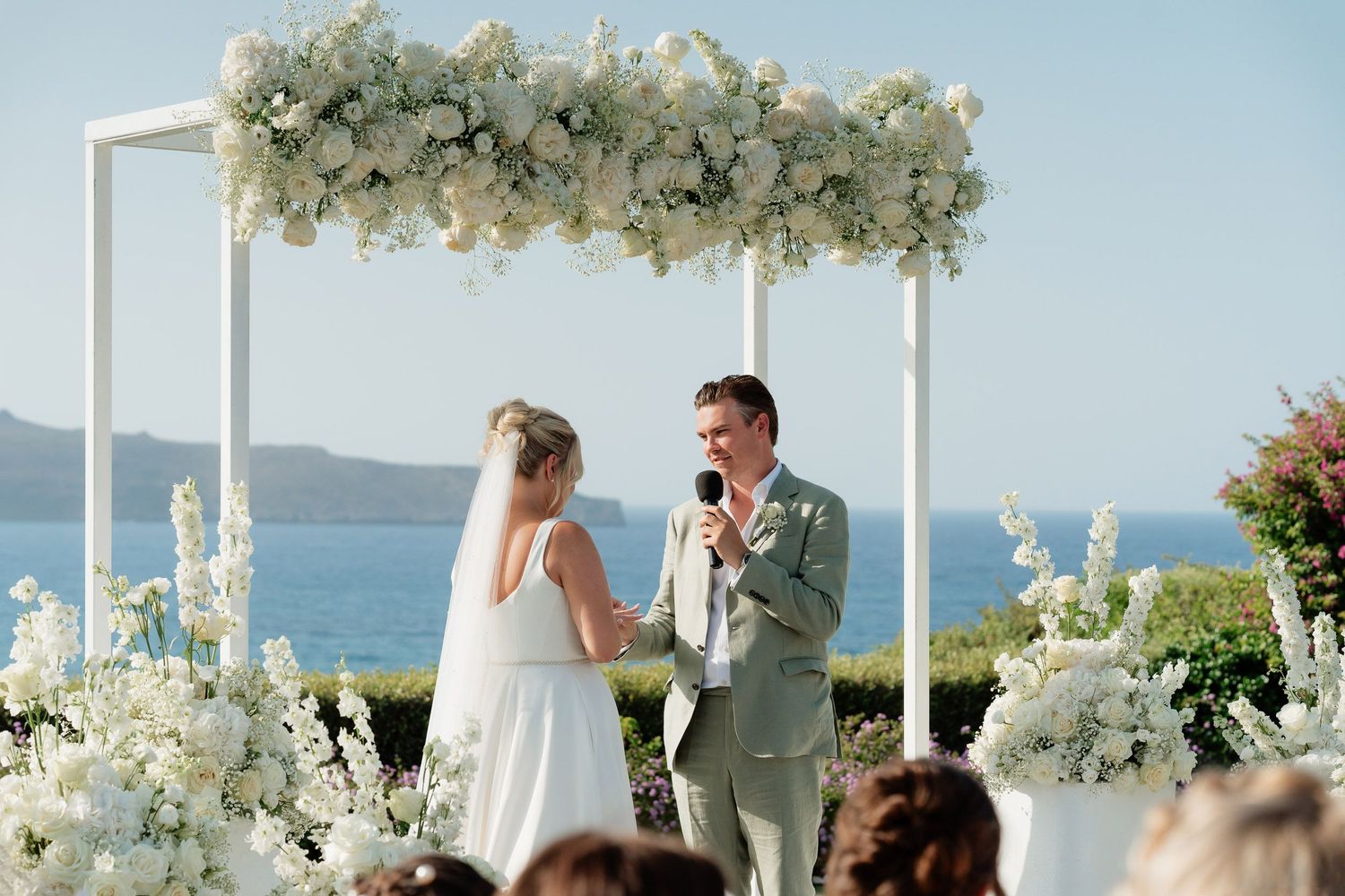 A beautiful seaside wedding ceremony setup with white floral arrangements and a coastal backdrop.