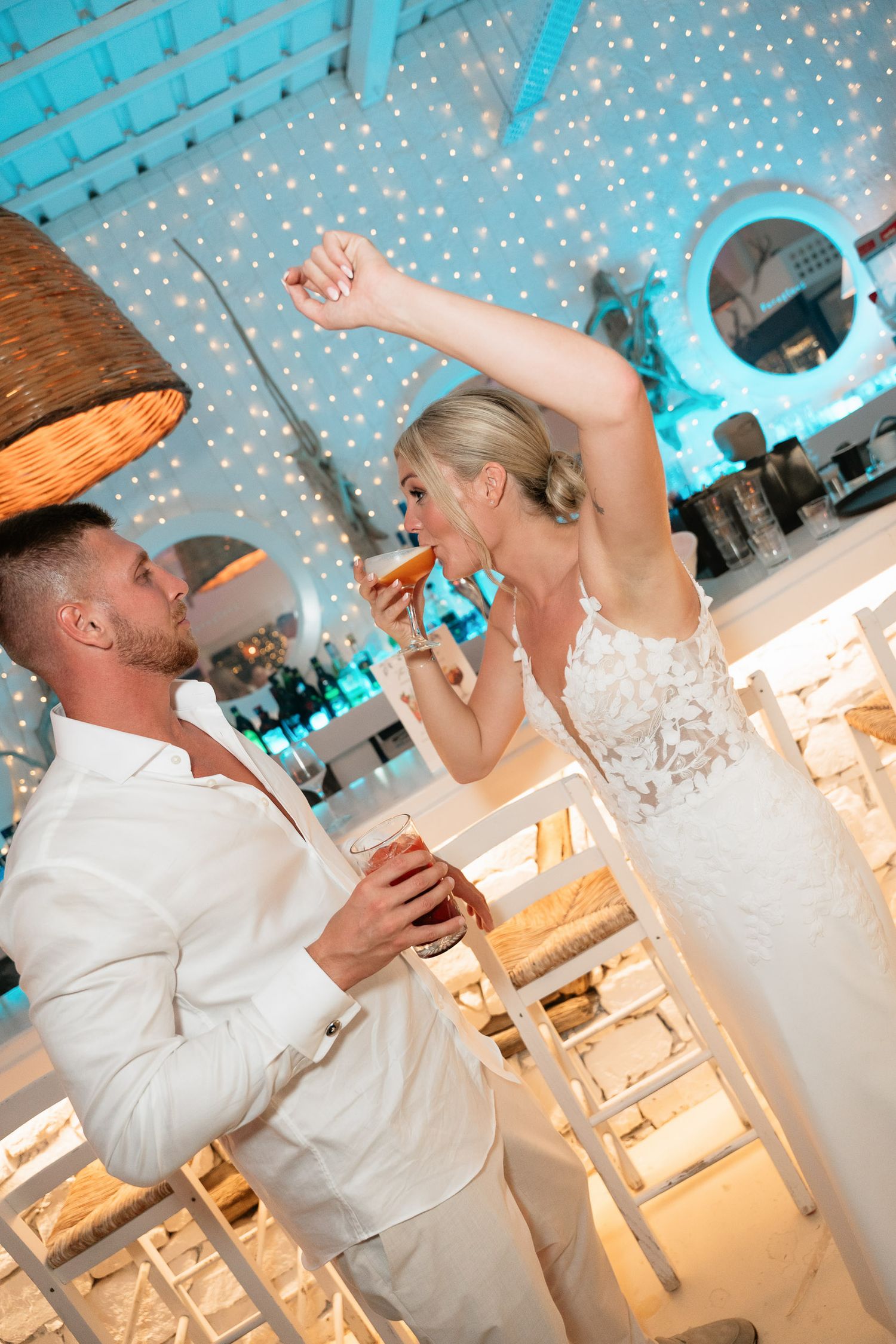 A couple shares a playful moment during their wedding reception under twinkling lights and turquoise decor.
