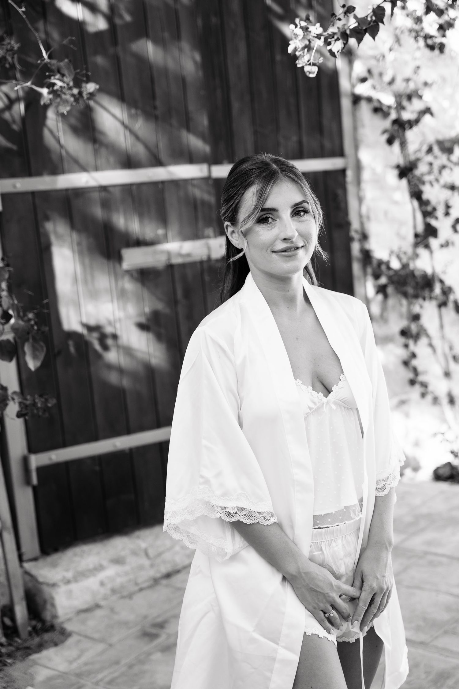 A person in a white dress poses in a black and white photo series against a dark wooden wall outdoors.