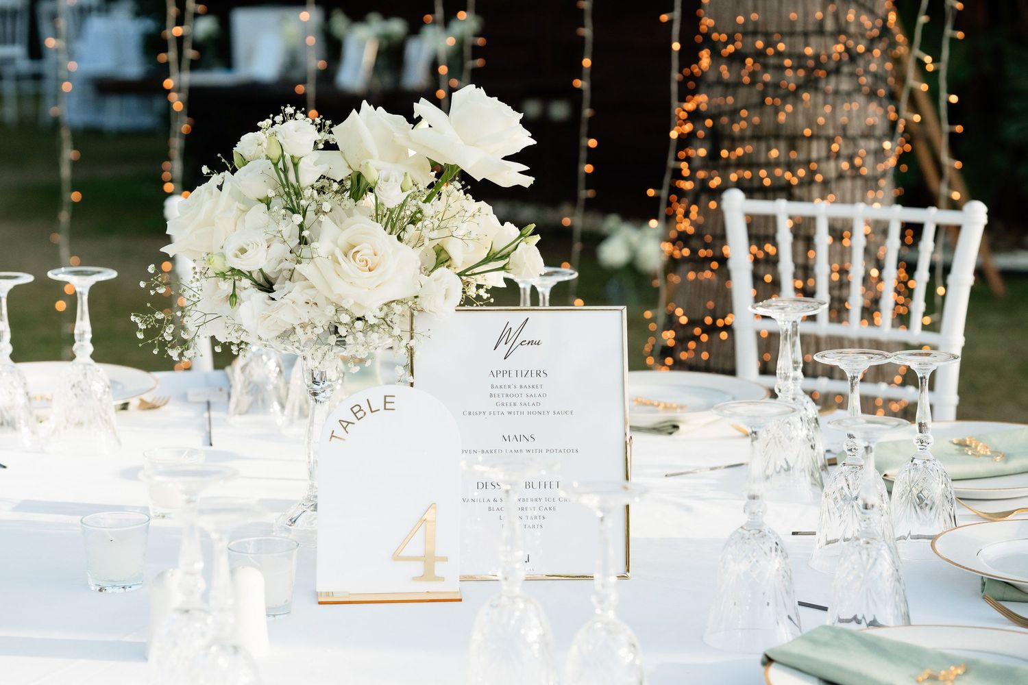 Elegant wedding reception tables decorated with white floral centerpieces and taper candles in a romantic outdoor setting.