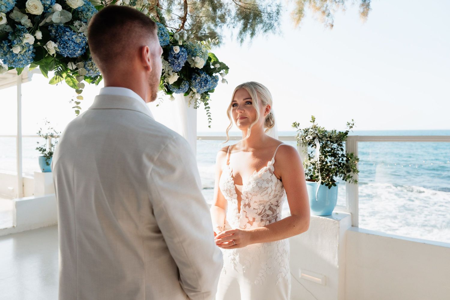 A couple exchanges vows during a seaside wedding ceremony under a floral arch with ocean views.