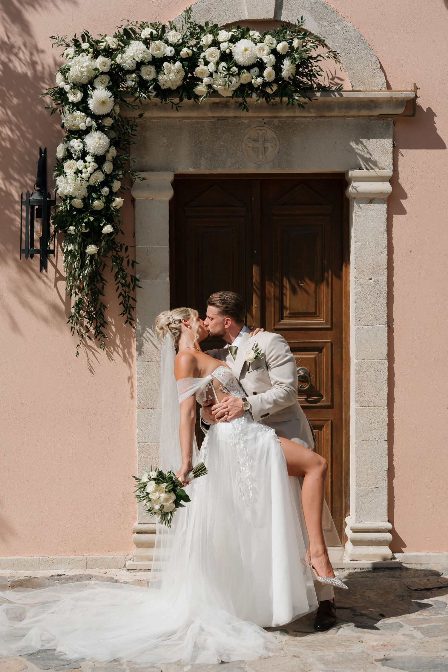 Elegant floral arch with white roses frames a romantic wedding moment at a Mediterranean-style doorway.