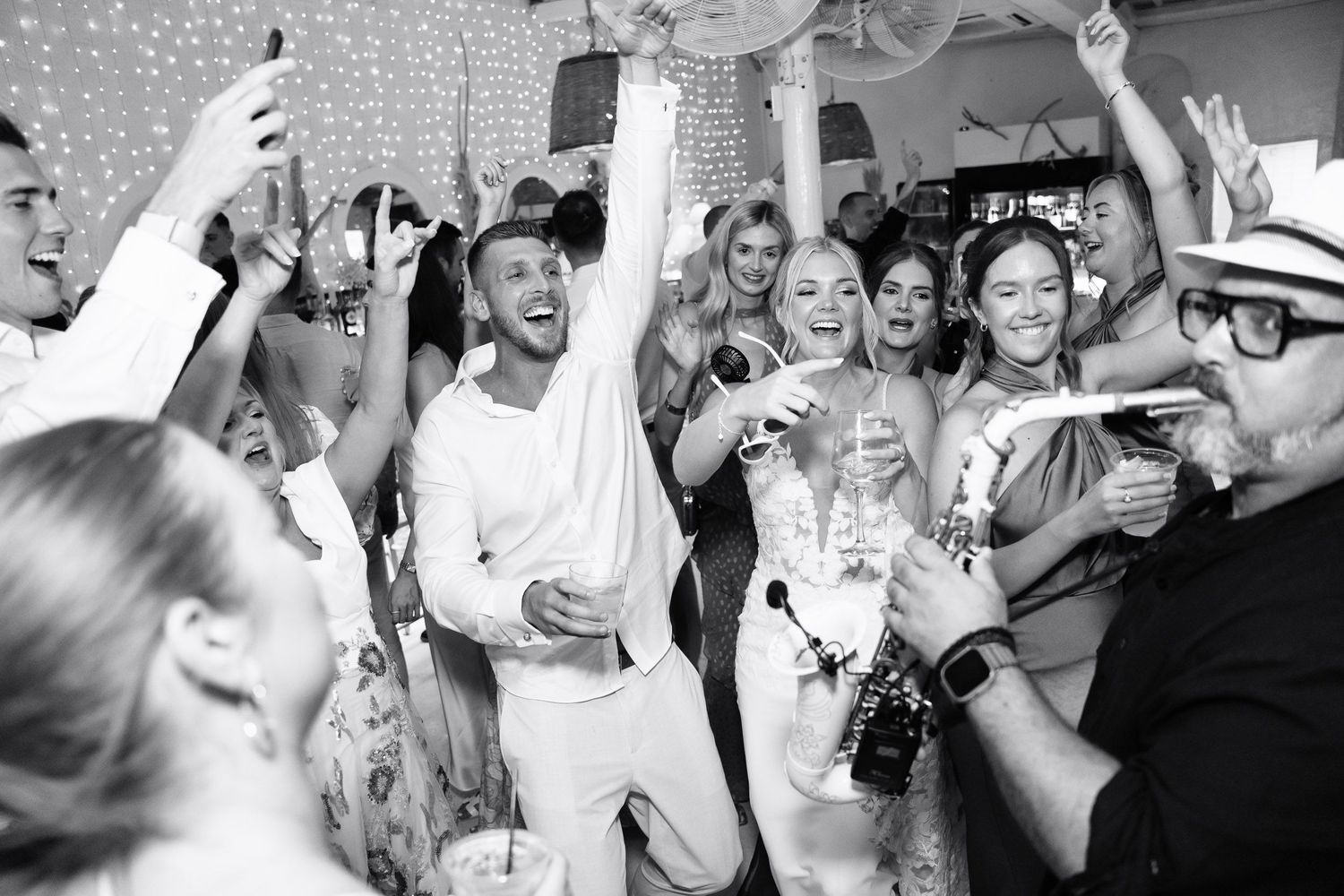 A lively black and white photo of people dancing and celebrating at a party with confetti and sparkles in the air.