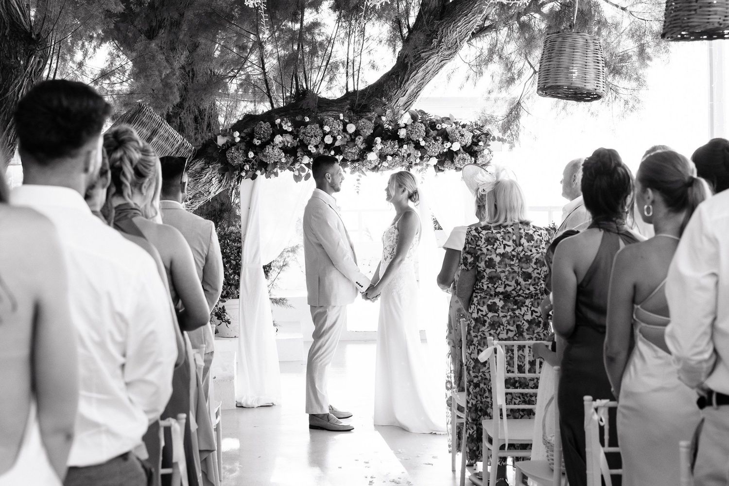 Black and white photo of an outdoor wedding ceremony under a tree with guests gathered to witness the occasion.