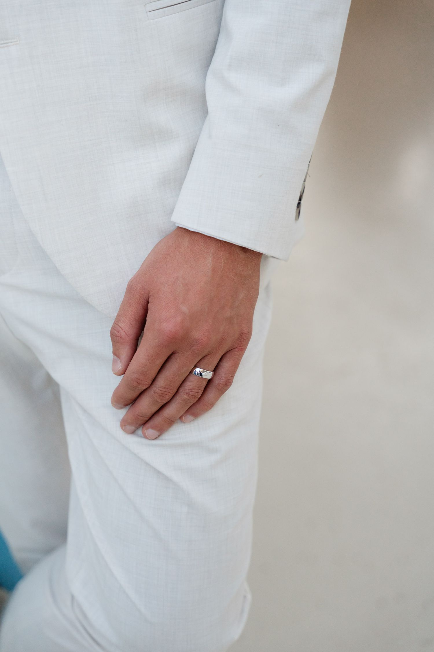 Close-up of a hand wearing a wedding ring against white formal attire.
