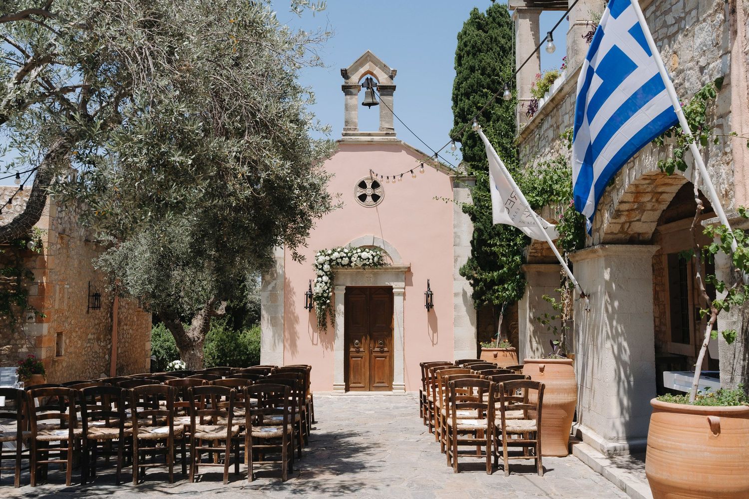 A rustic Mediterranean courtyard with olive trees and stone buildings featuring wooden doors and traditional architecture.