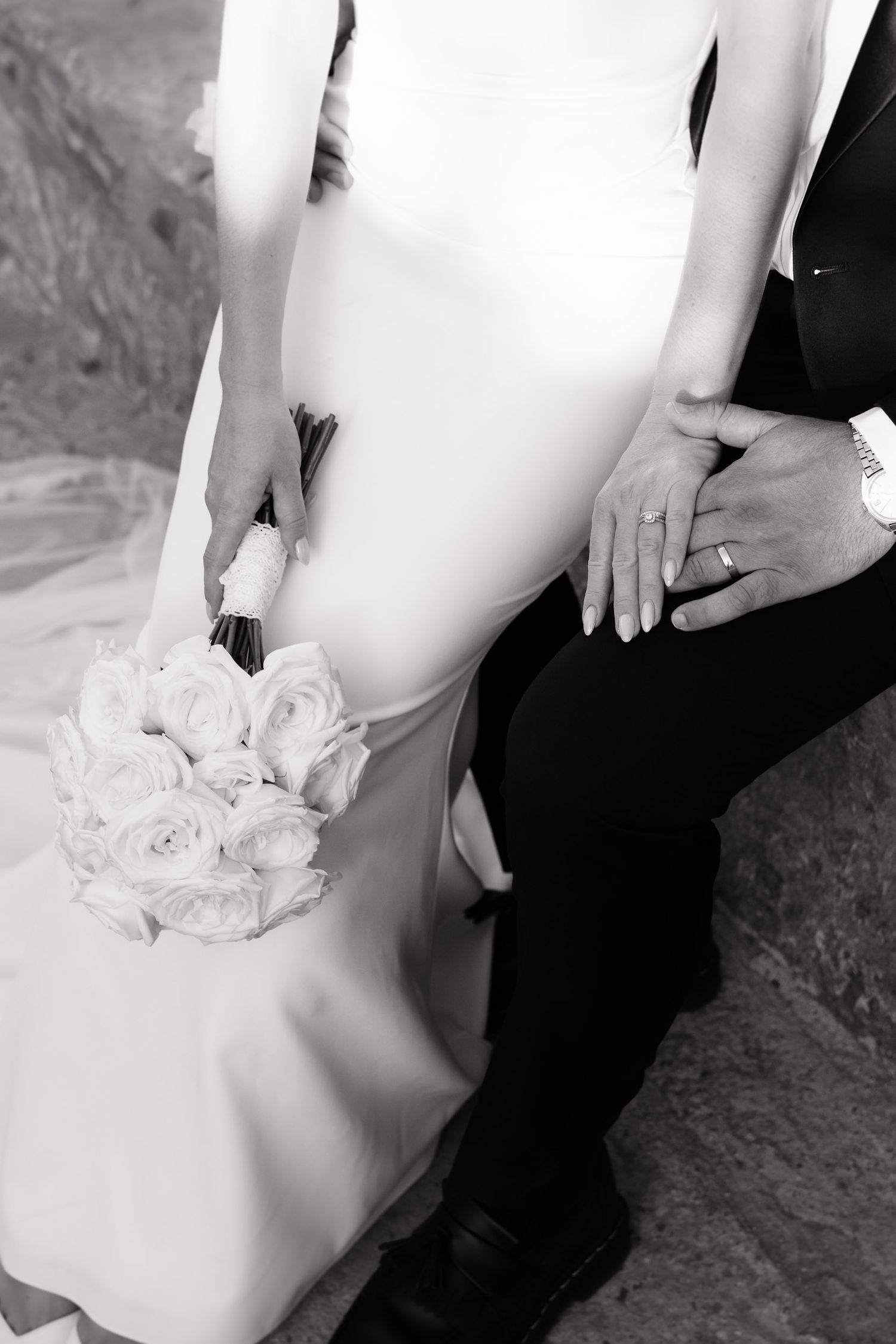 Black and white wedding photo series showing a couple's hands holding a white rose bouquet against formal attire.