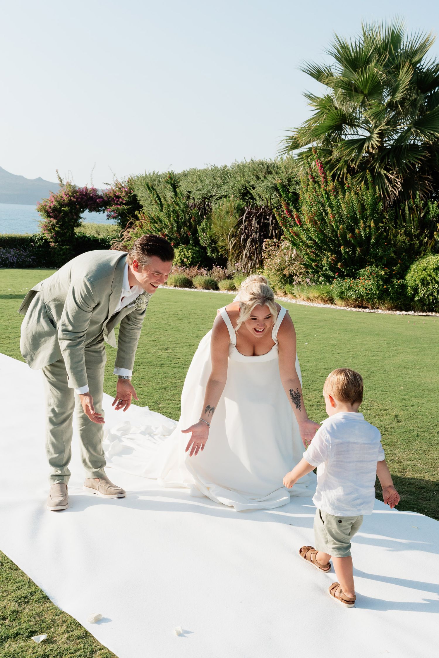 Wedding party members help straighten out a white fabric on grass lawn with palm trees in background.