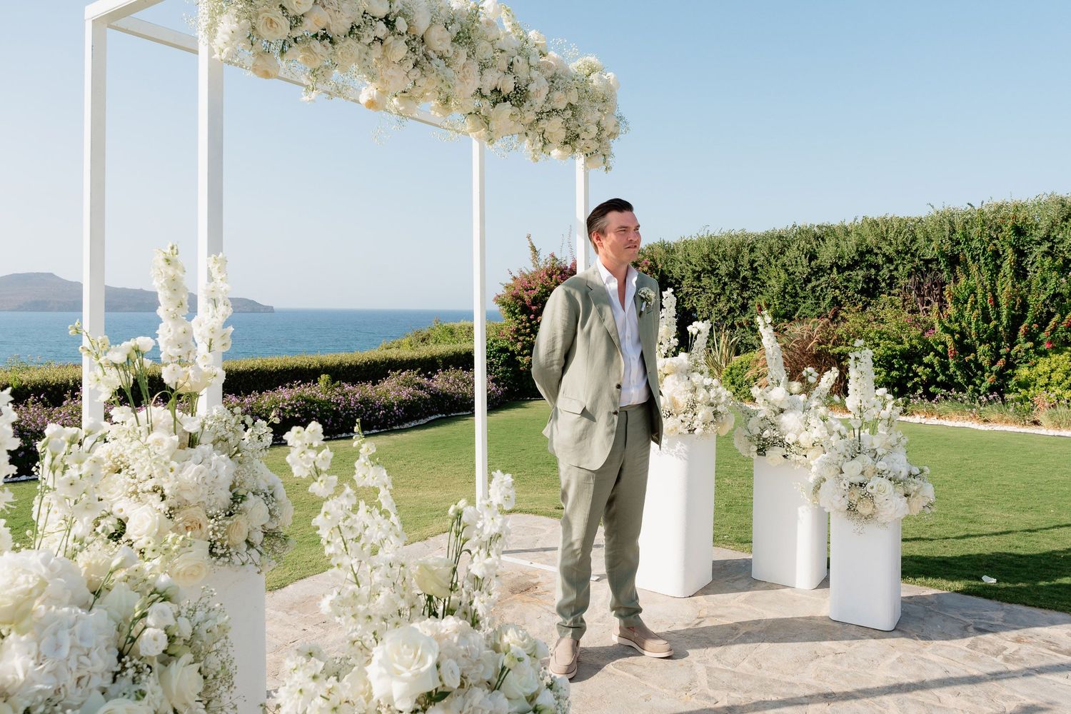Elegant outdoor wedding ceremony setup with white floral arrangements and ocean views in the background.