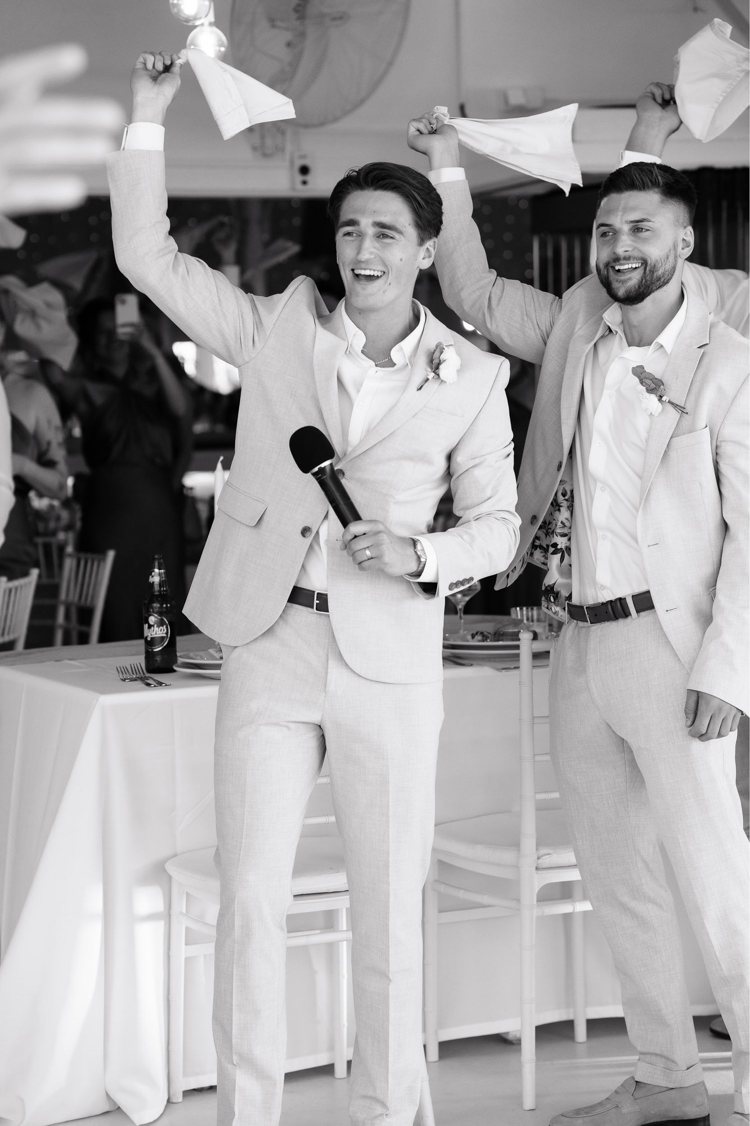 A group of groomsmen in all-white suits dance and celebrate during a wedding reception.