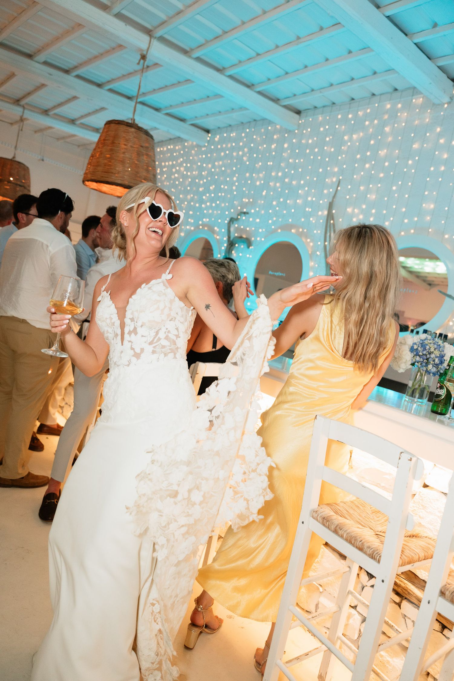 Party guests dance and celebrate at a reception venue decorated with twinkling fairy lights and turquoise ceiling accents.