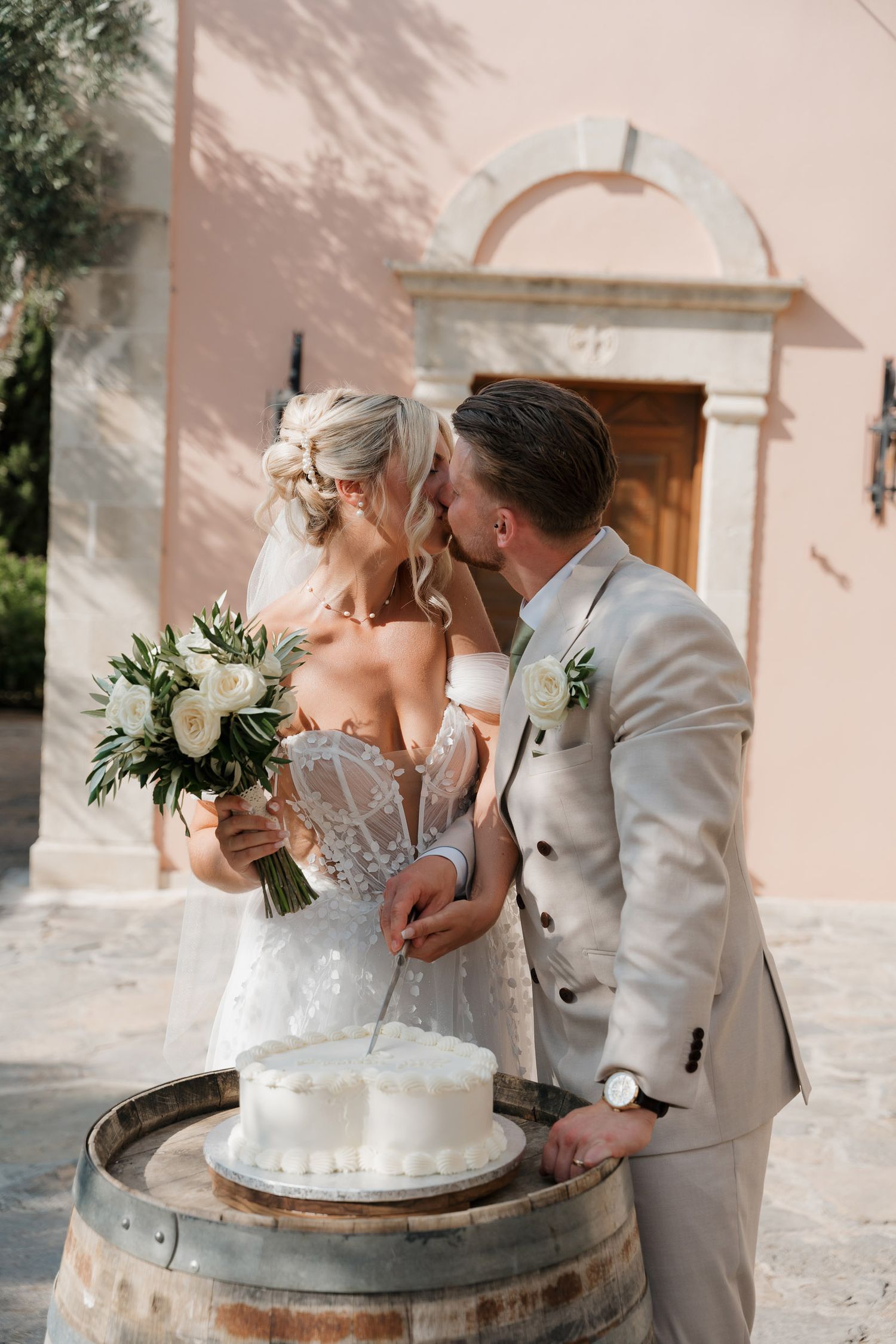 Romantic wedding couple sharing intimate moments and kisses while posing with their wedding cake on rustic wine barrel.