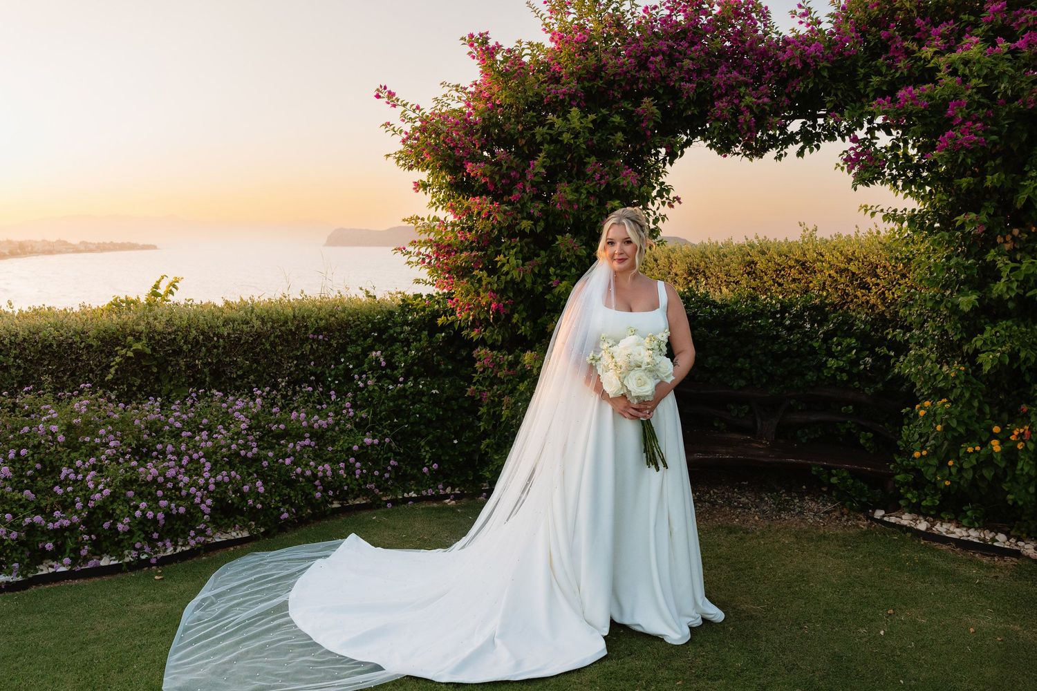 A flowing white wedding dress billows in the breeze against a scenic garden backdrop during golden hour.