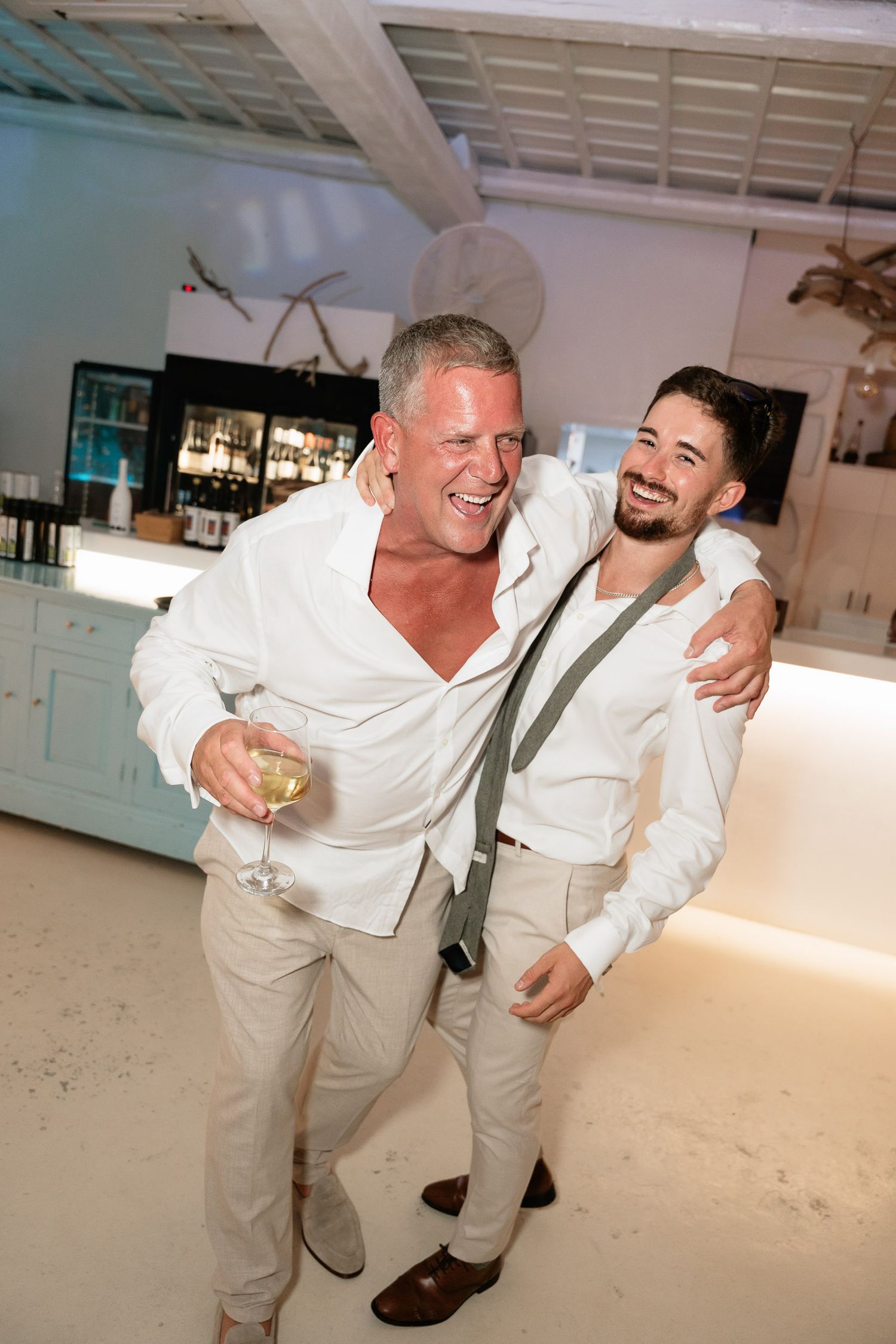 Two people in white outfits share a joyful moment dancing and laughing together in a bright indoor space.