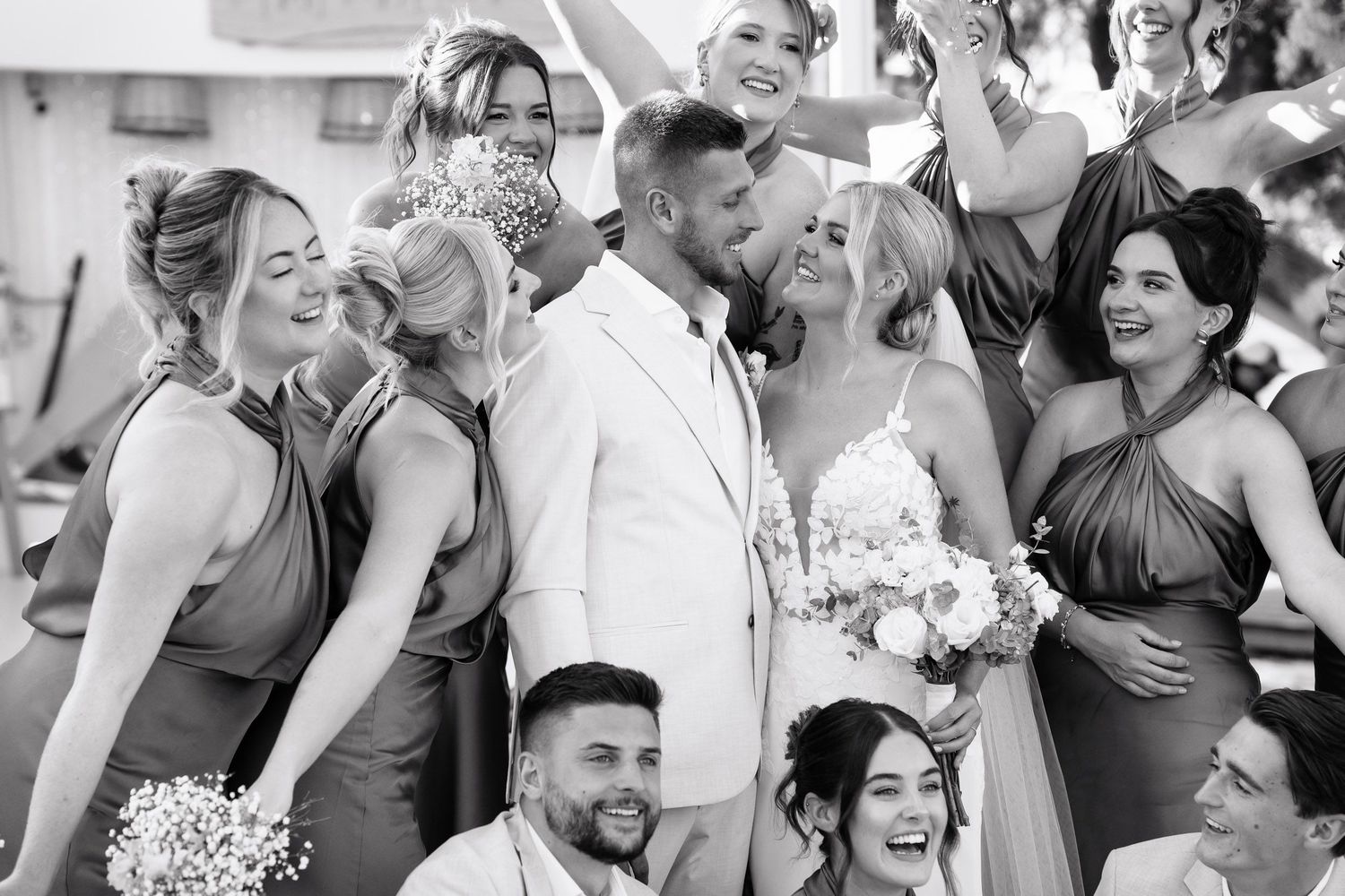 A joyful wedding party laughs together during outdoor celebration photos.