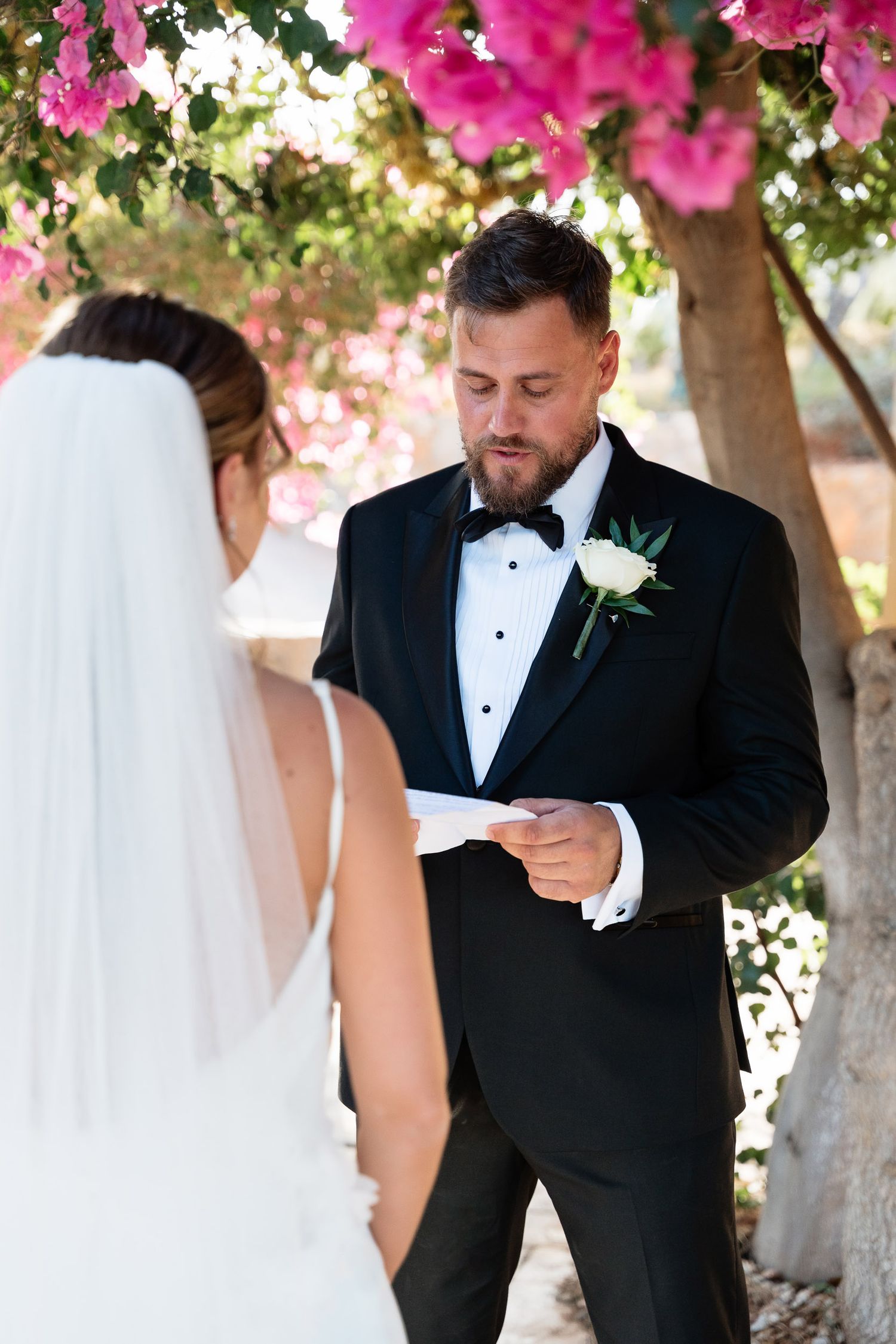 A couple shares an intimate moment under blooming pink bougainvillea during their wedding ceremony.