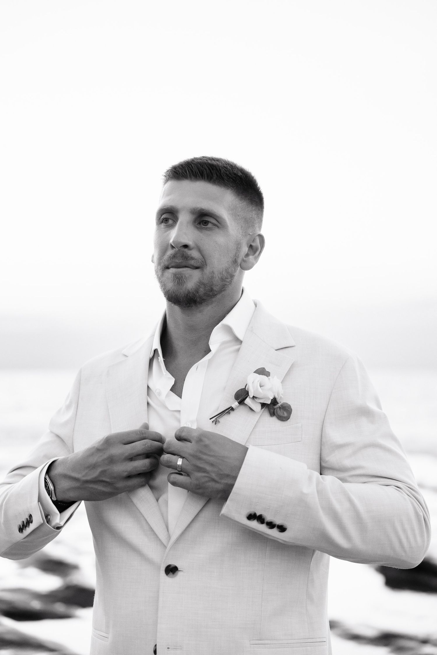 Close-up sequence of groom adjusting his white suit jacket and boutonniere on the beach.