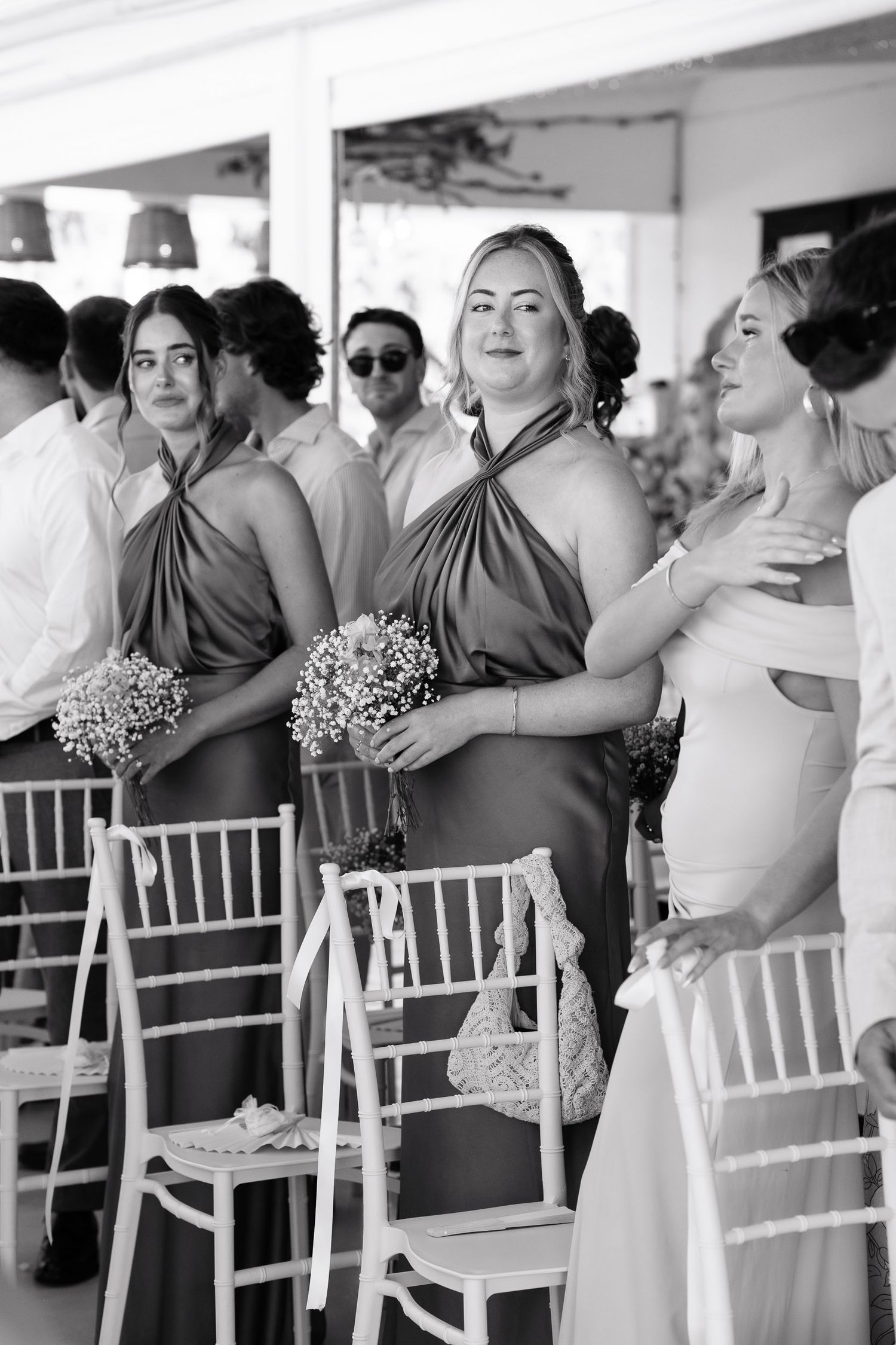 A black and white photo of wedding guests seated in white chairs under a tent during an outdoor reception.