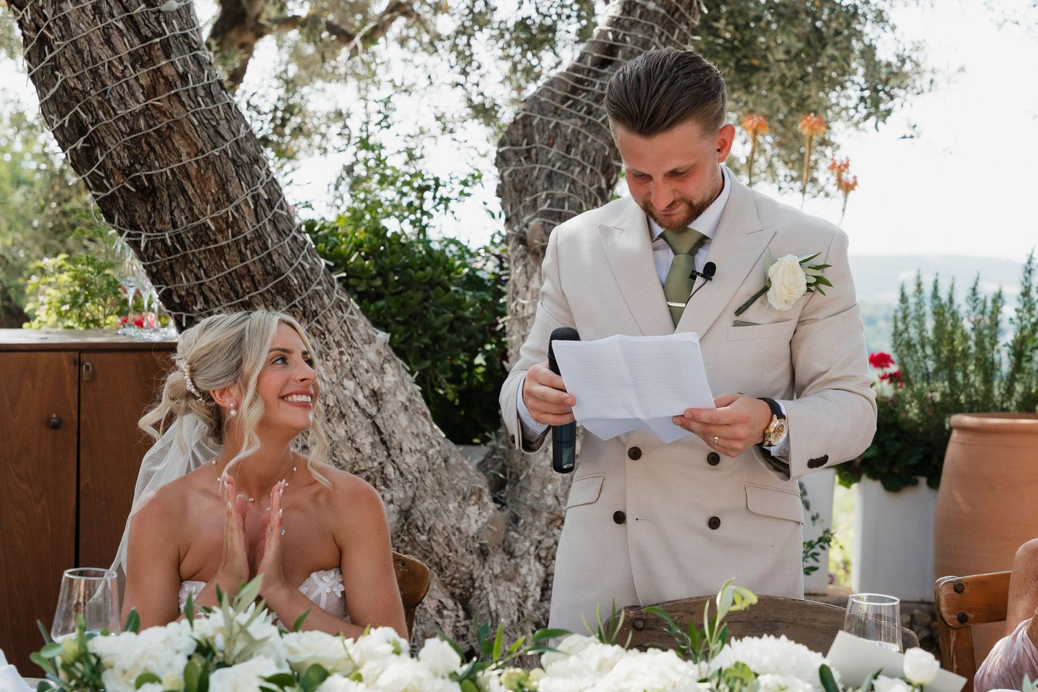 A couple shares an emotional moment during their outdoor wedding ceremony under olive trees in a Mediterranean setting.