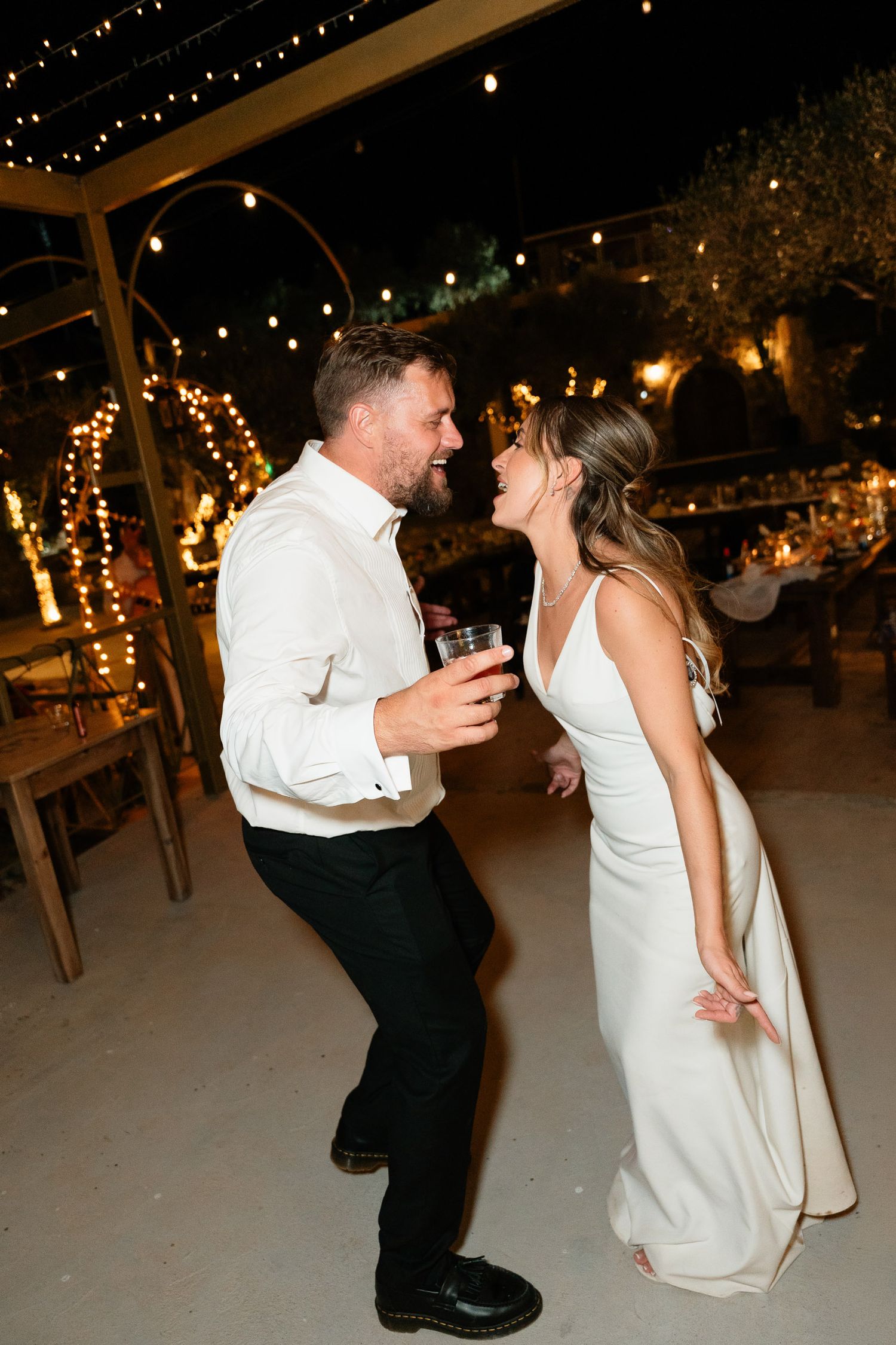 A couple shares a romantic dance dip during their wedding reception under twinkling string lights.