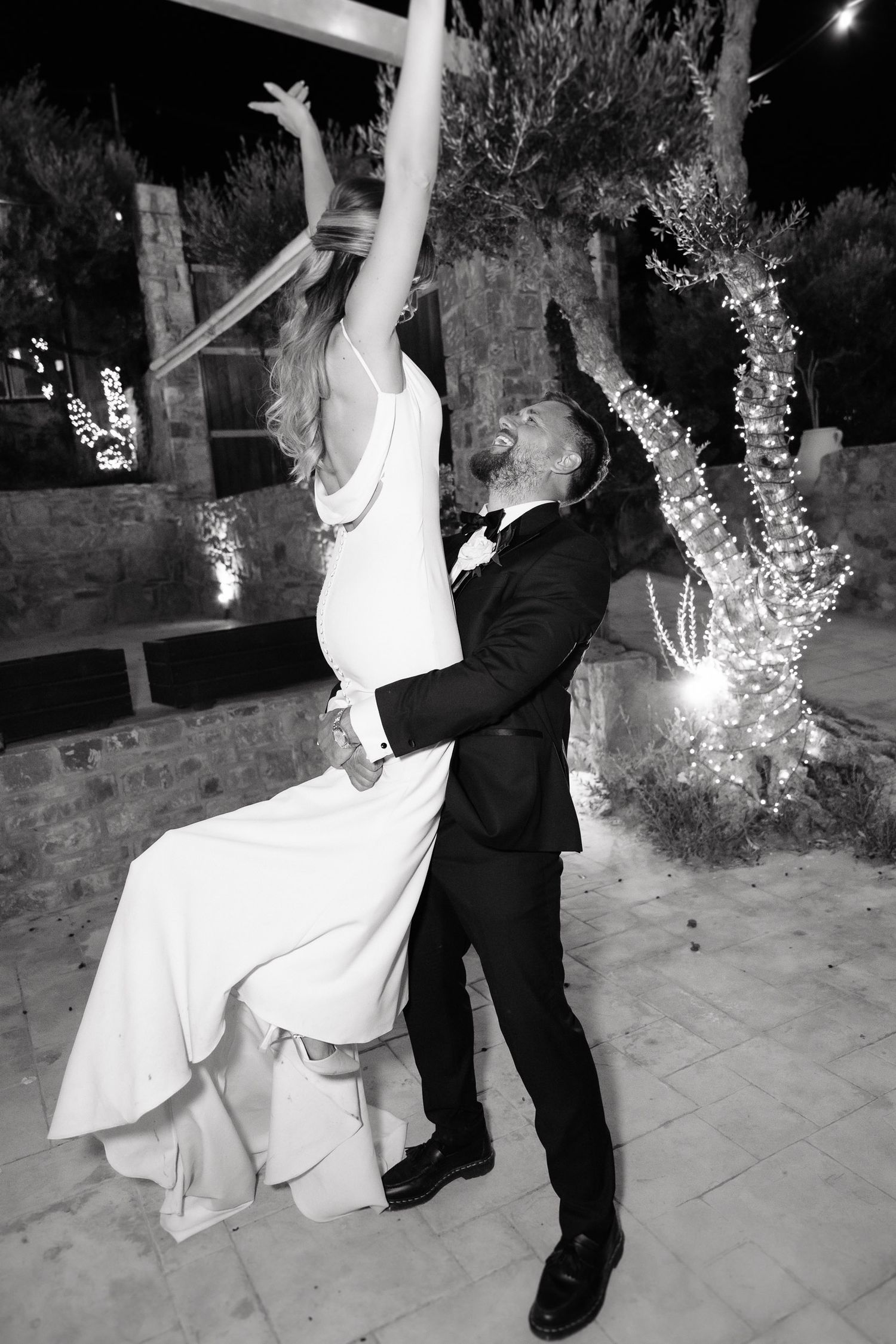 A couple performs a romantic dip dance move during a wedding celebration at night with illuminated trees in the background.