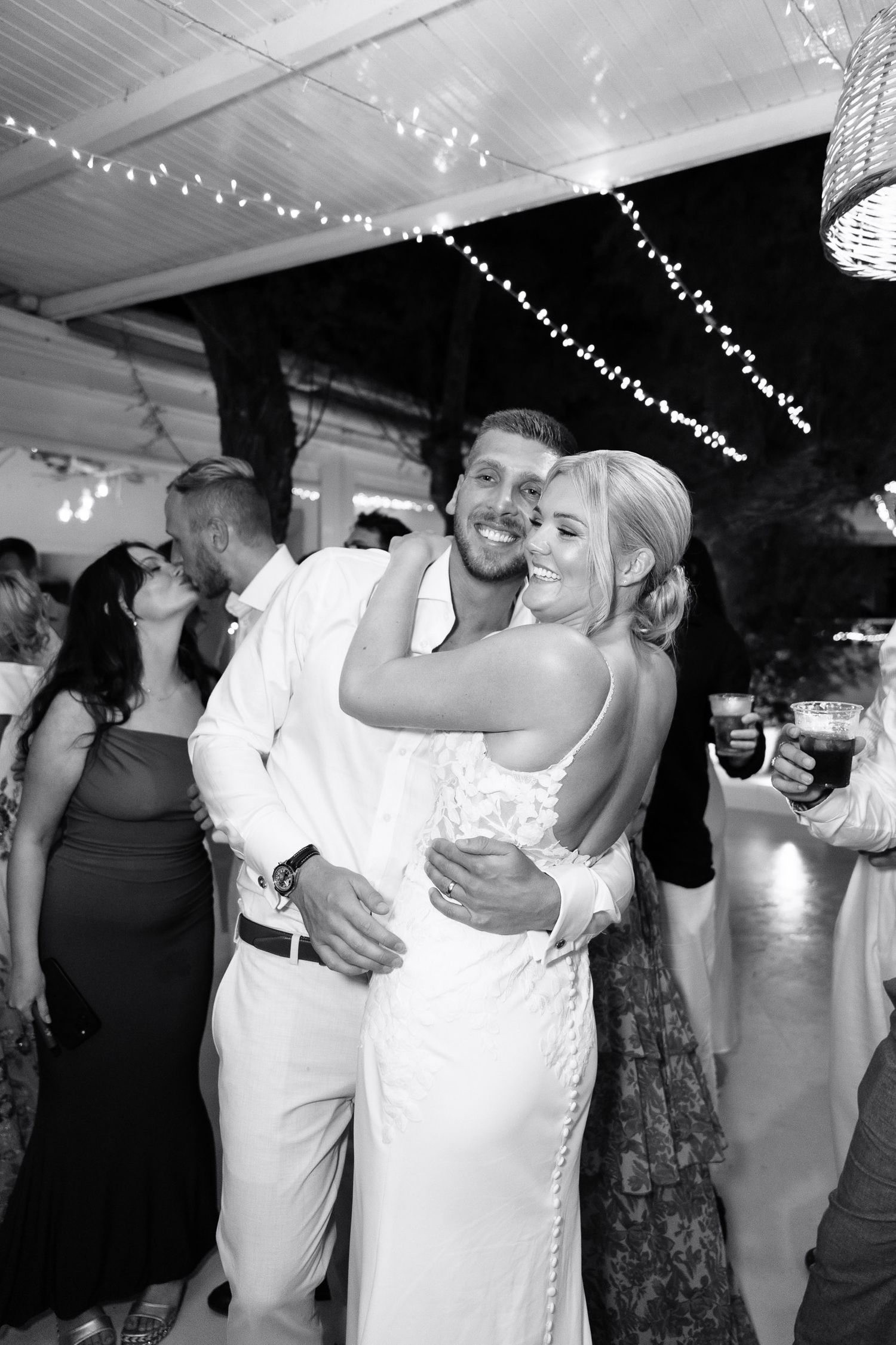 Couples dance together at a wedding reception under string lights in a black and white photo series.