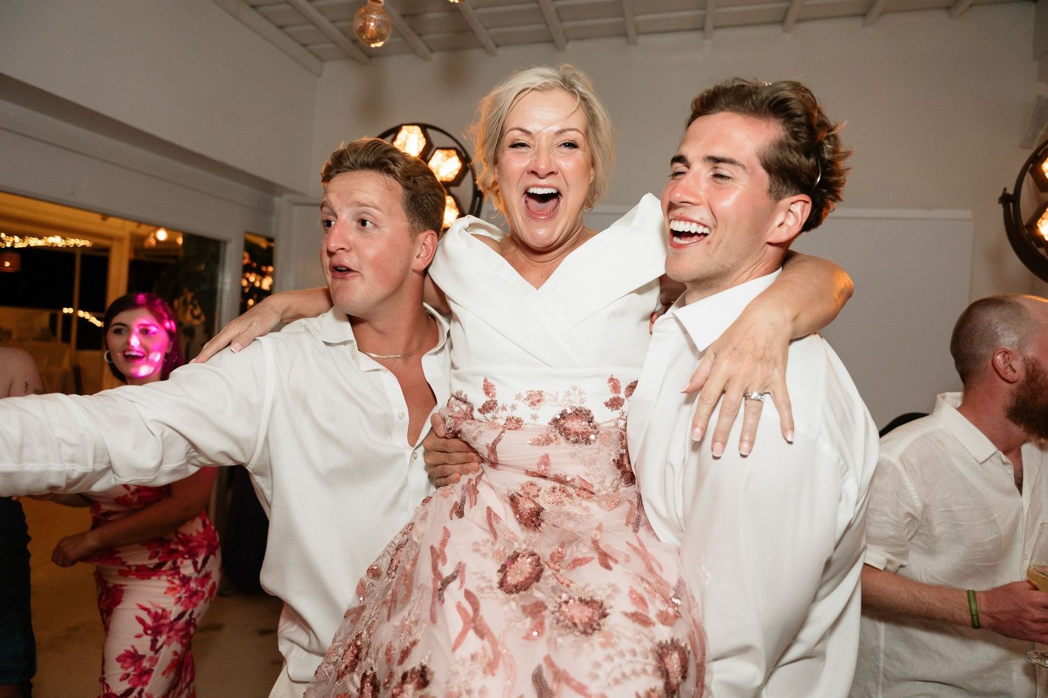 Joyful wedding guests dance and celebrate together on the dance floor at an indoor reception venue.