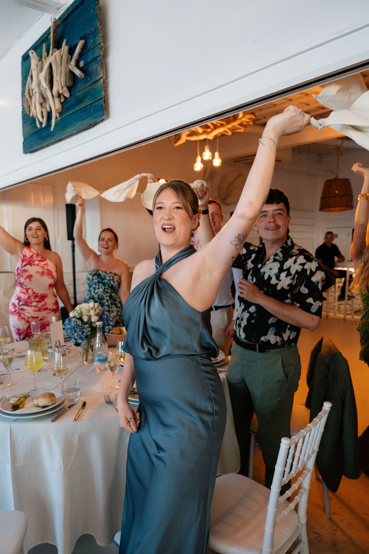 Wedding guests celebrate and dance together at a reception with white tablecloths and teal decor.