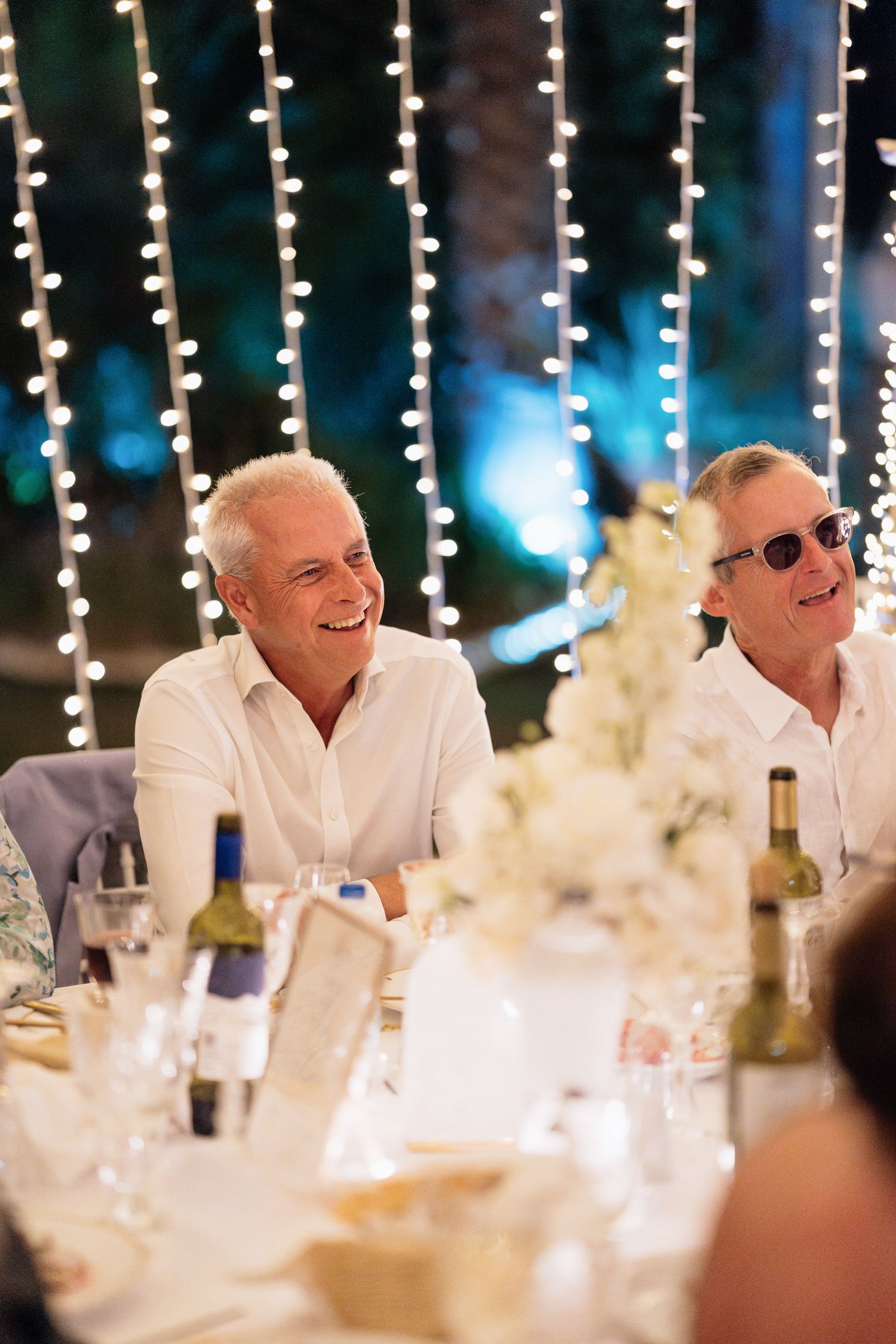 People seated at an elegant wedding reception dinner table with hanging string lights creating a romantic atmosphere.
