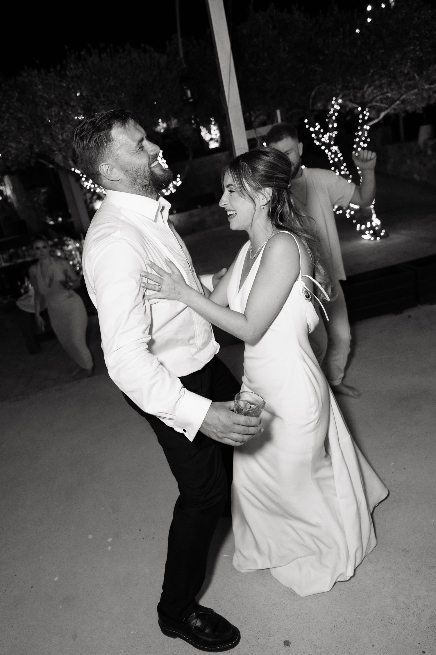 A black and white photo series captures a couple dancing at a wedding reception with joyful energy and movement.