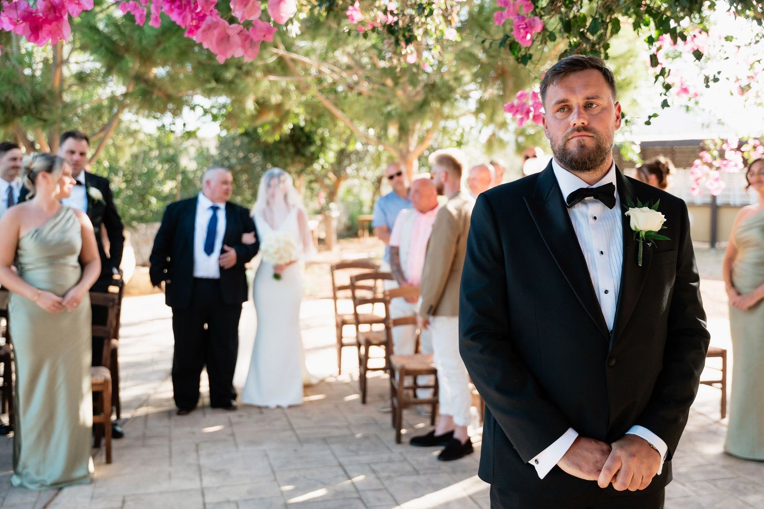 A group of wedding guests dancing and celebrating at an outdoor reception under trees.