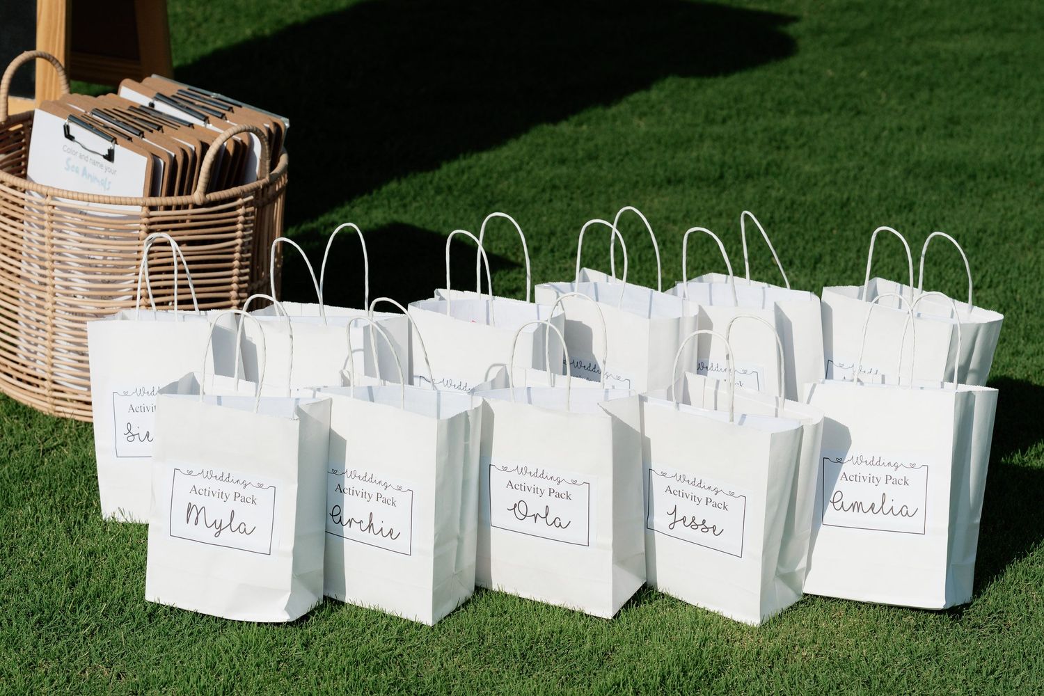 White paper gift bags with handles arranged in rows on green grass outdoors.