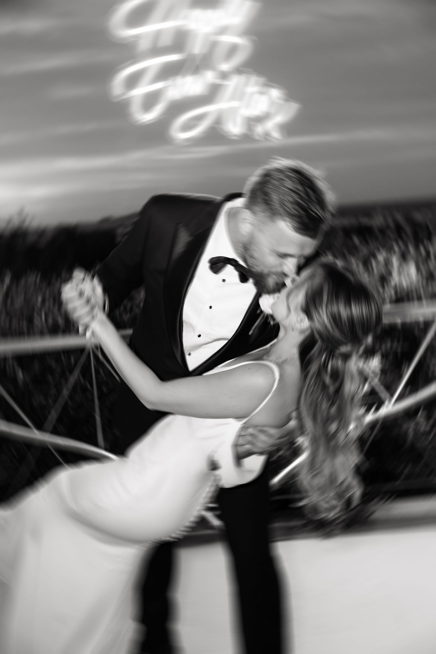 Black and white photo of bride and groom sharing a romantic dip kiss during their first dance at wedding reception.