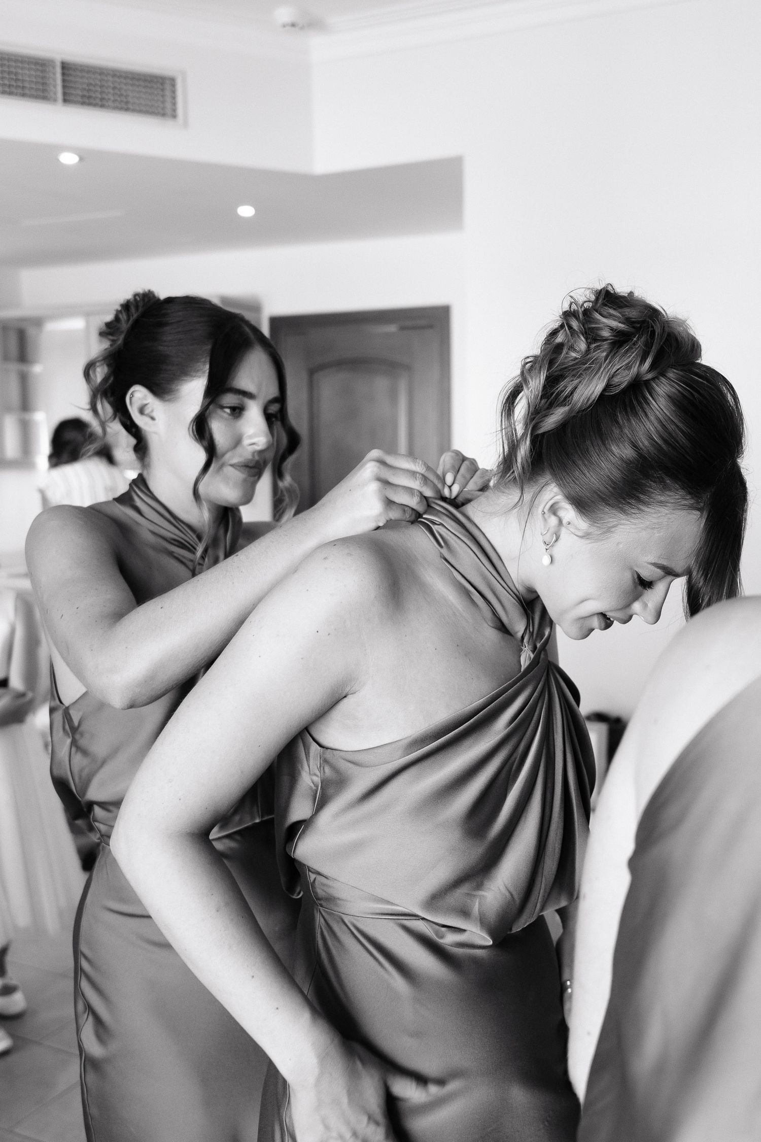 A series of black and white photos showing bridesmaids helping each other get dressed in matching gowns.
