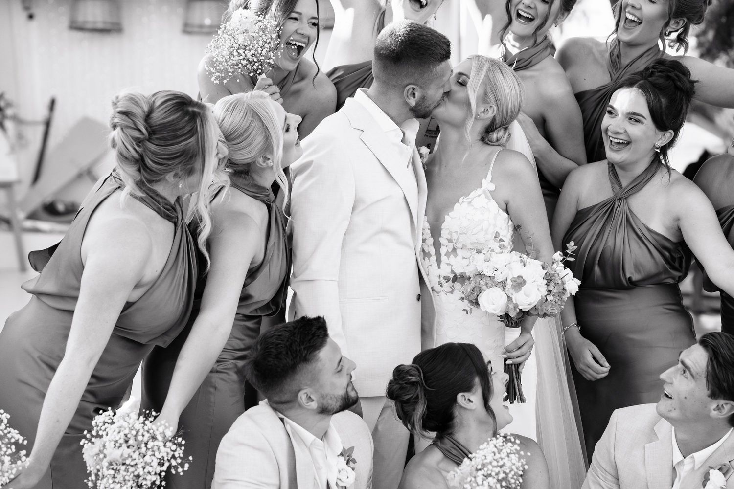 A joyful wedding party shares a candid moment of laughter together in black and white photography.