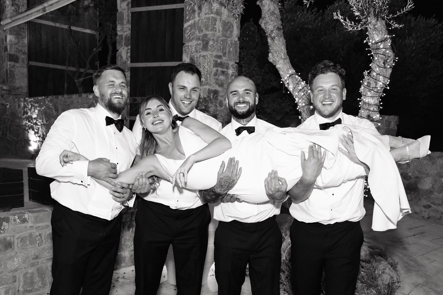 A group of groomsmen in white dress shirts pose playfully while celebrating at a wedding reception.