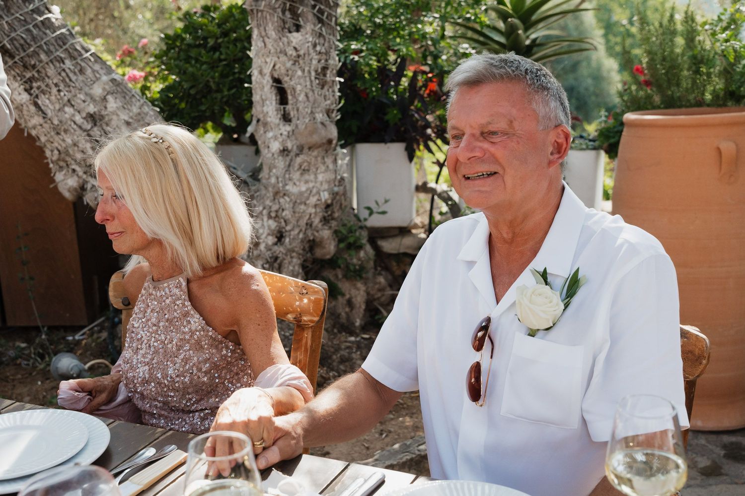 Two people enjoying an outdoor meal at a table with wine glasses and place settings on a sunny day.