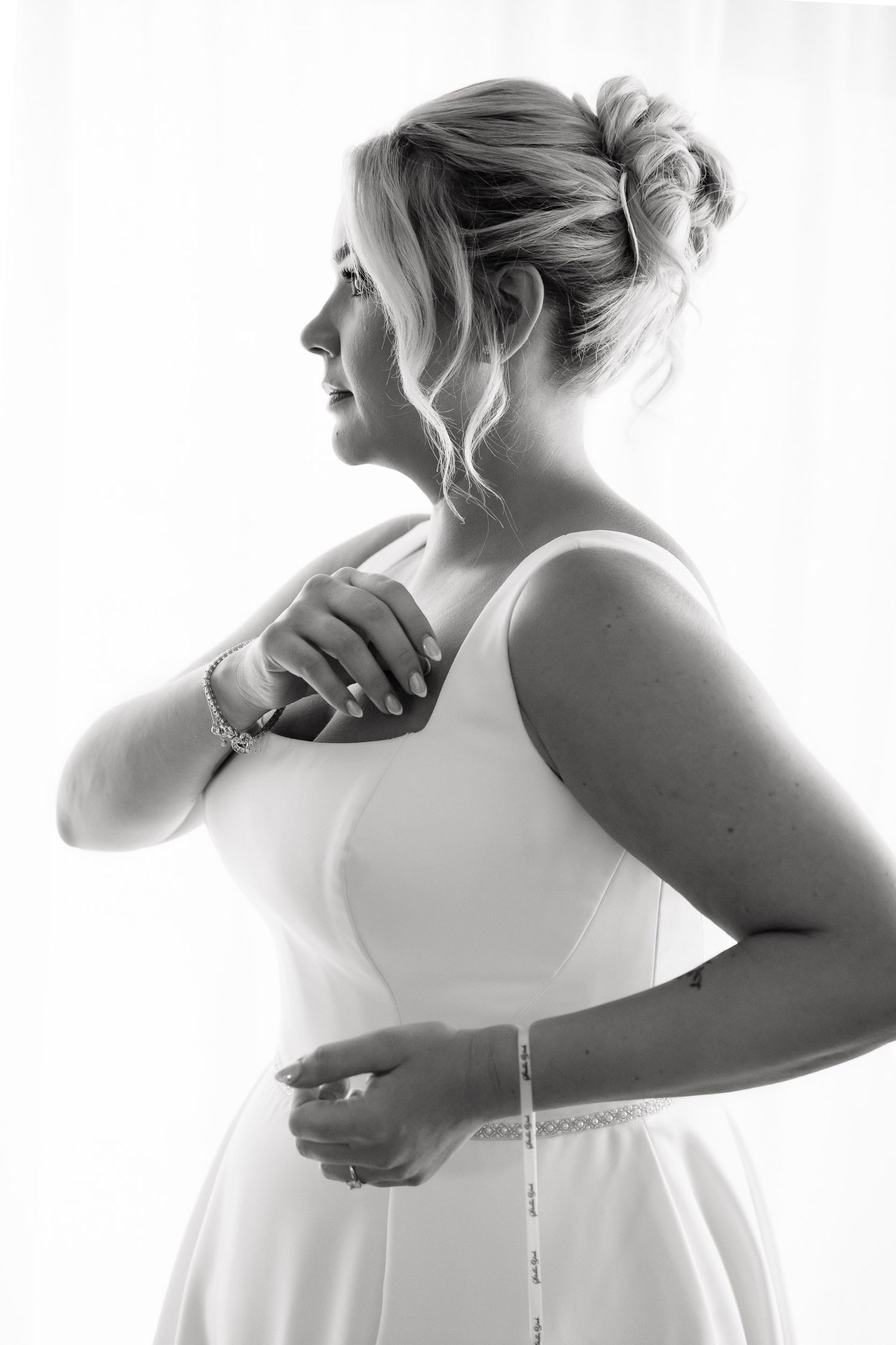 A series of black and white photos showing someone getting dressed in a white wedding gown.