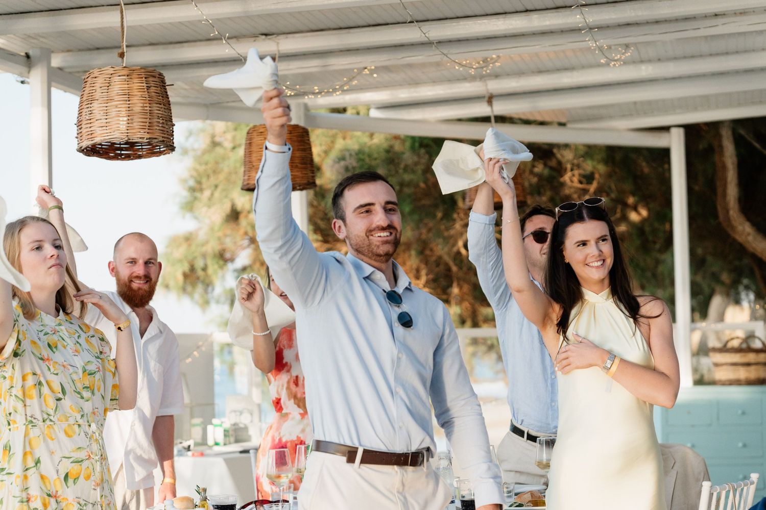 Wedding guests dance and celebrate together during an outdoor reception with hanging wicker lanterns and string lights.