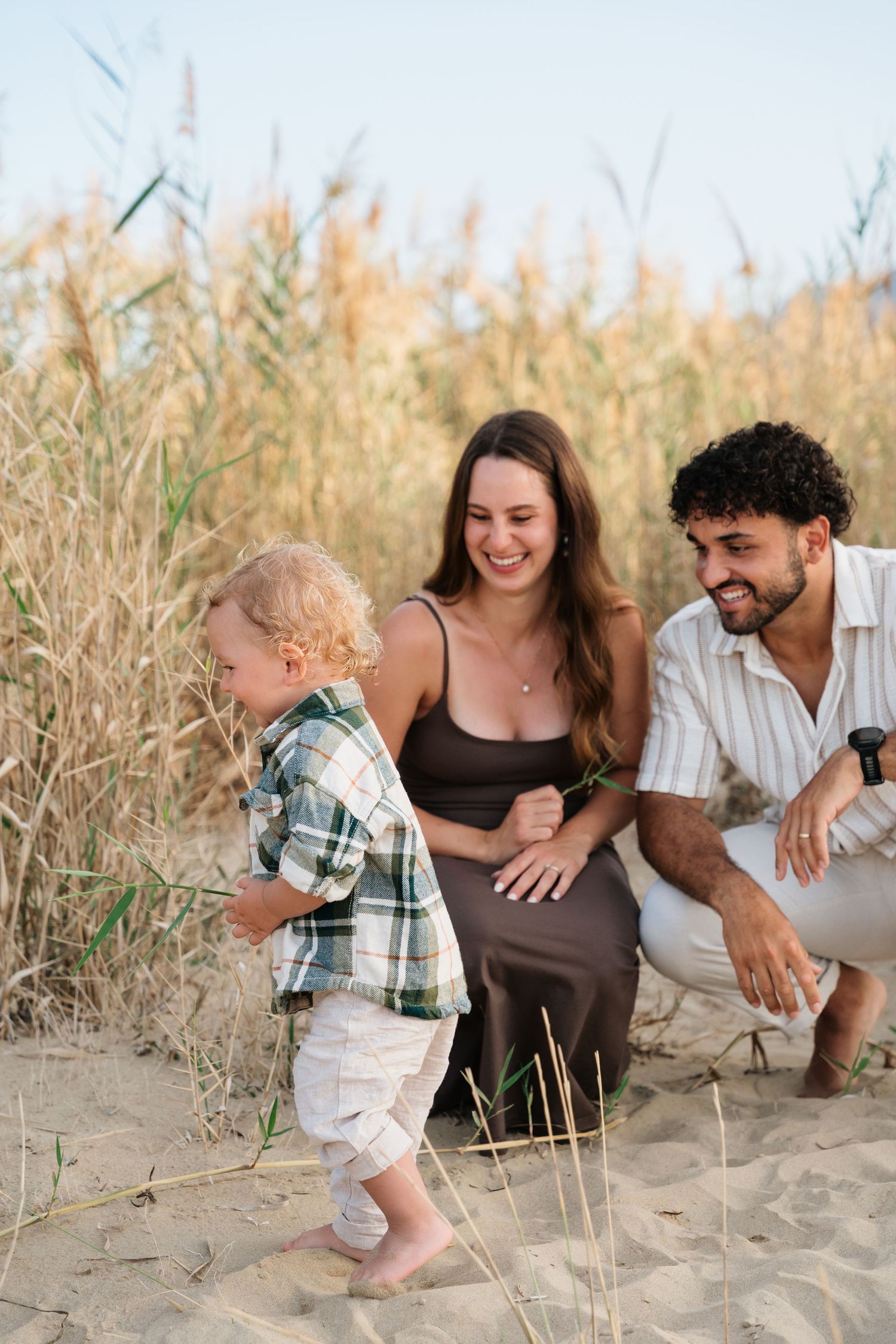 A family shares joyful moments together while sitting in tall beach grass during a sunset photoshoot.