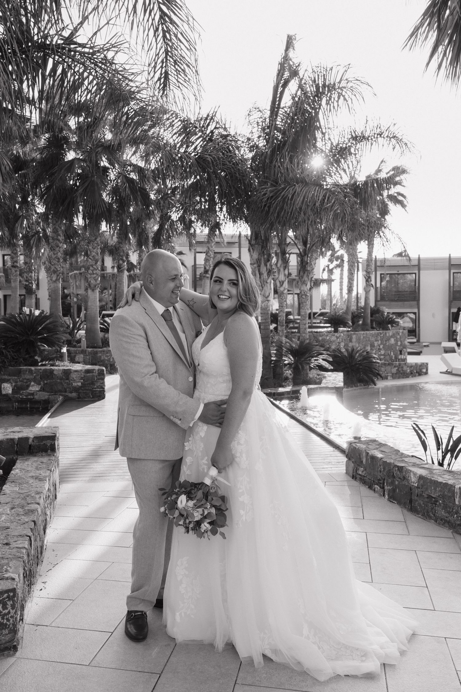 Black and white wedding photograph of couple posing by a tropical resort pool at Stella Island Resort, Crete