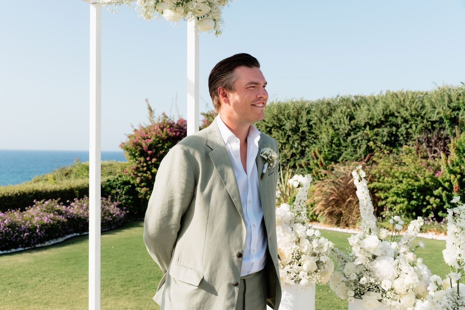 A couple shares a romantic moment in a garden setting by the ocean on their wedding day.