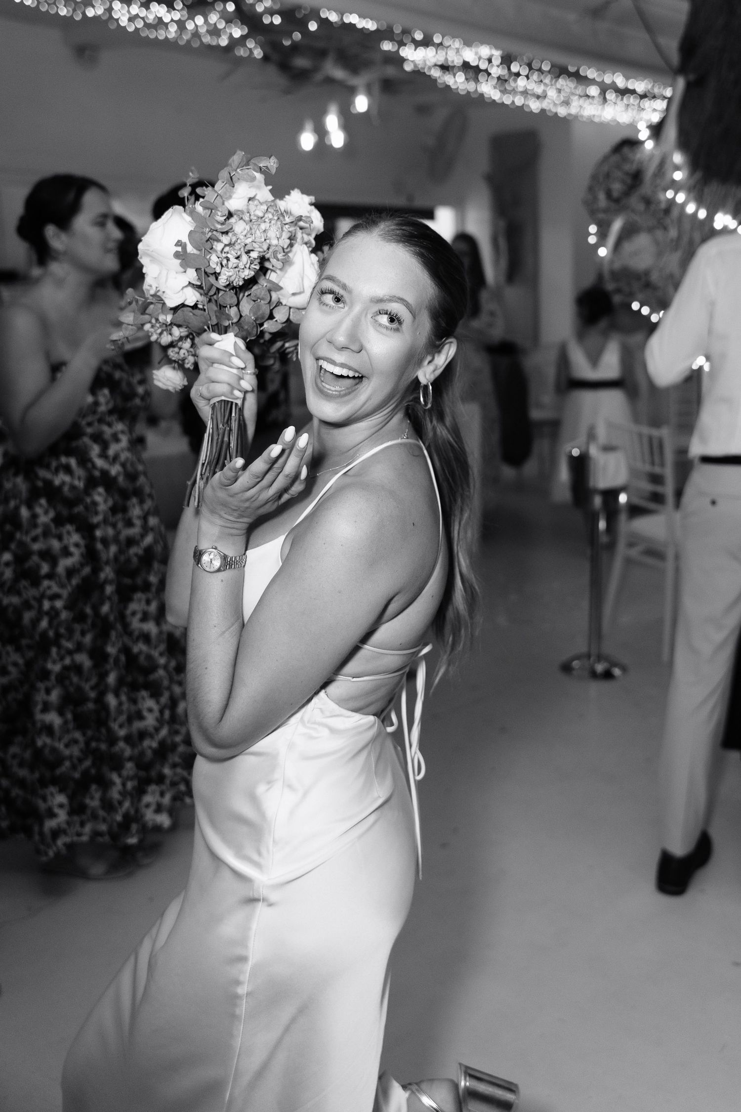 A series of black and white photos showing a bride in a white dress laughing and posing at a wedding reception.