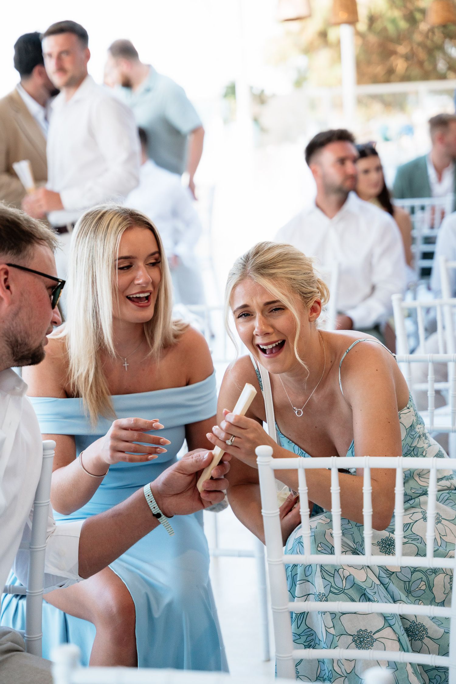Wedding guests share a lighthearted moment at an outdoor reception while wearing light blue attire.