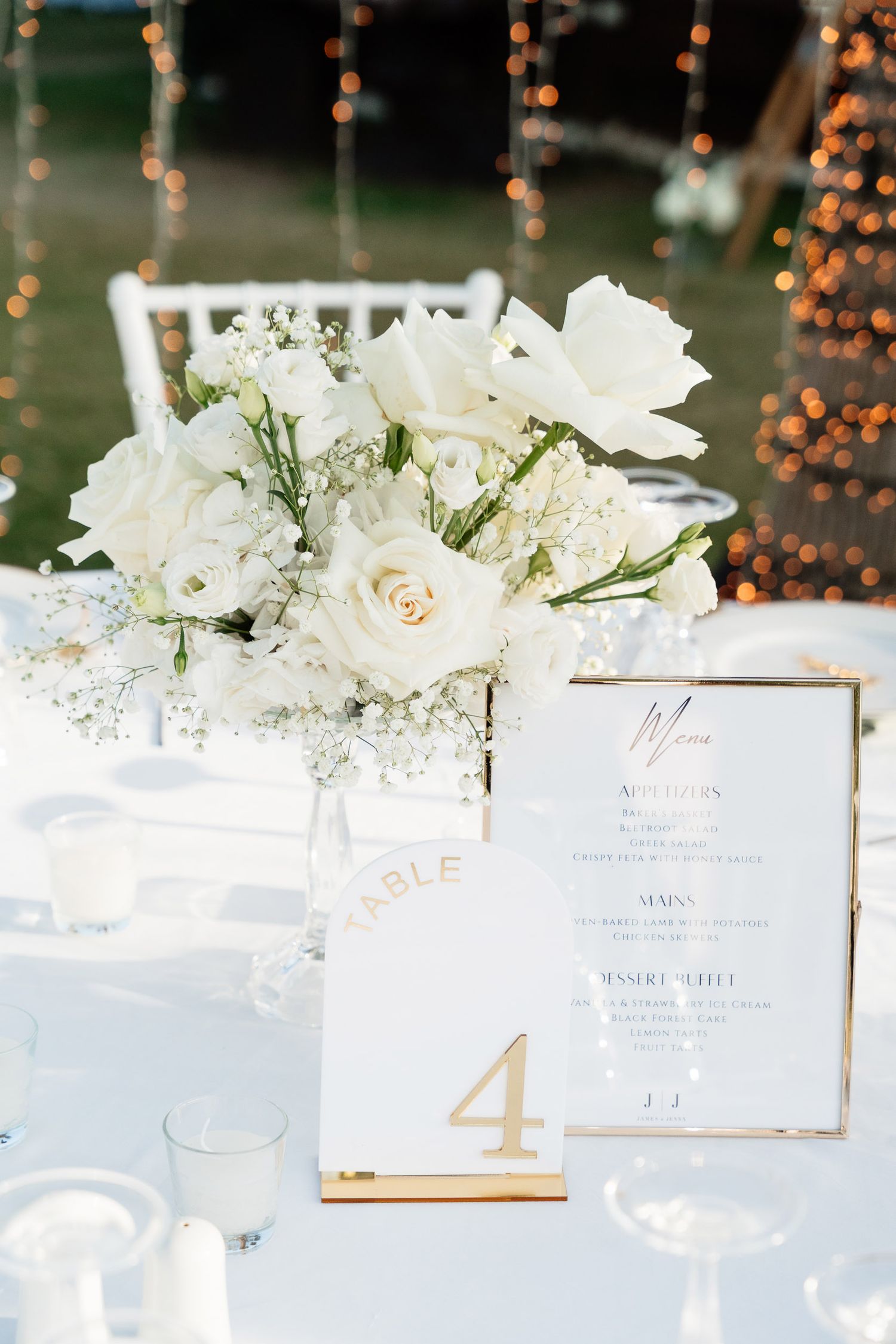 Elegant wedding table decor with white floral arrangements and gold table numbers on white tablecloths.