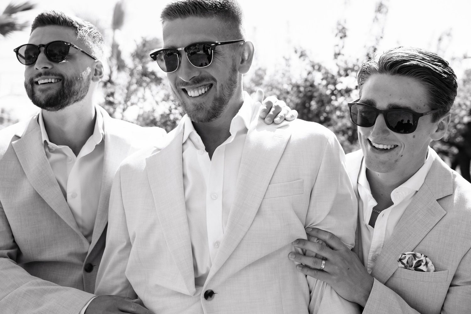 A group of people wearing white outfits and sunglasses smile together outdoors in a casual setting.