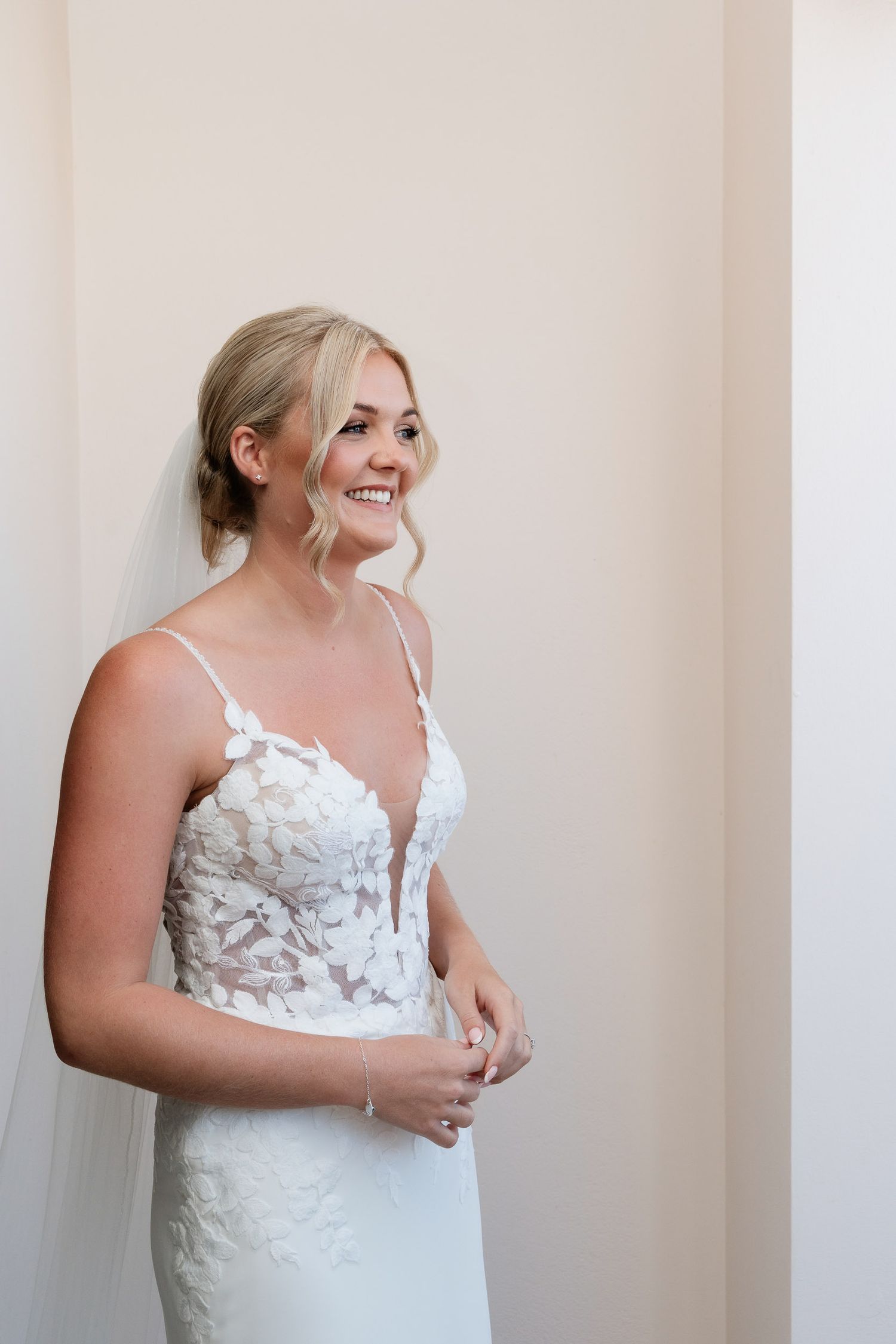 Bride wearing a strapless white wedding gown with floral appliques poses against a light colored wall in multiple shots.