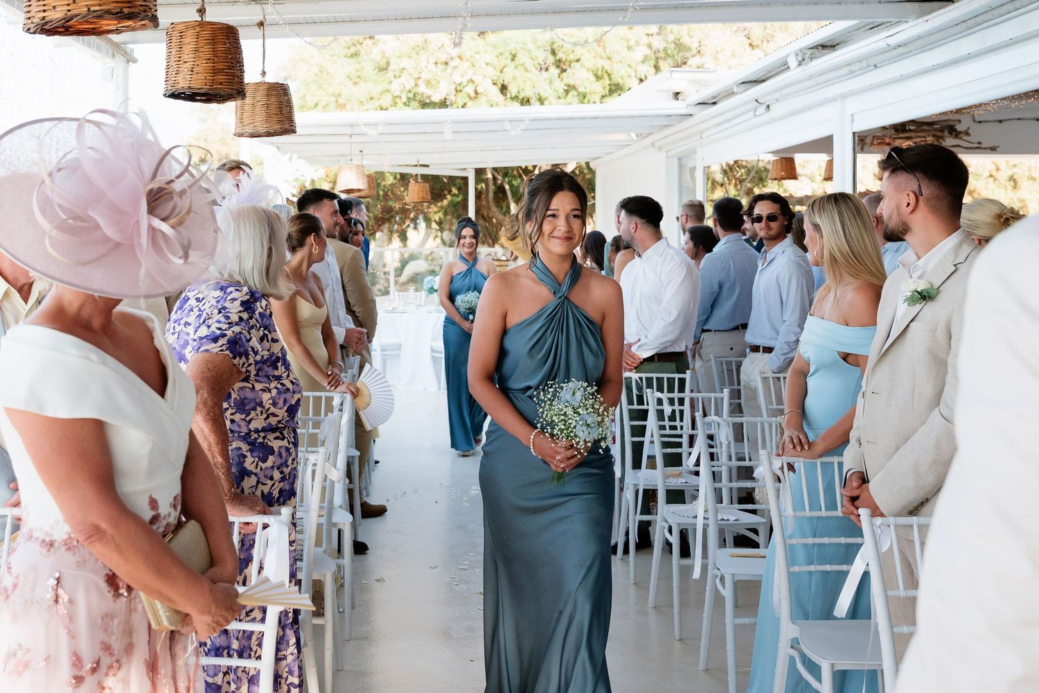 Wedding guests in light blue dresses gather at an elegant outdoor reception venue with white decor and hanging lanterns.