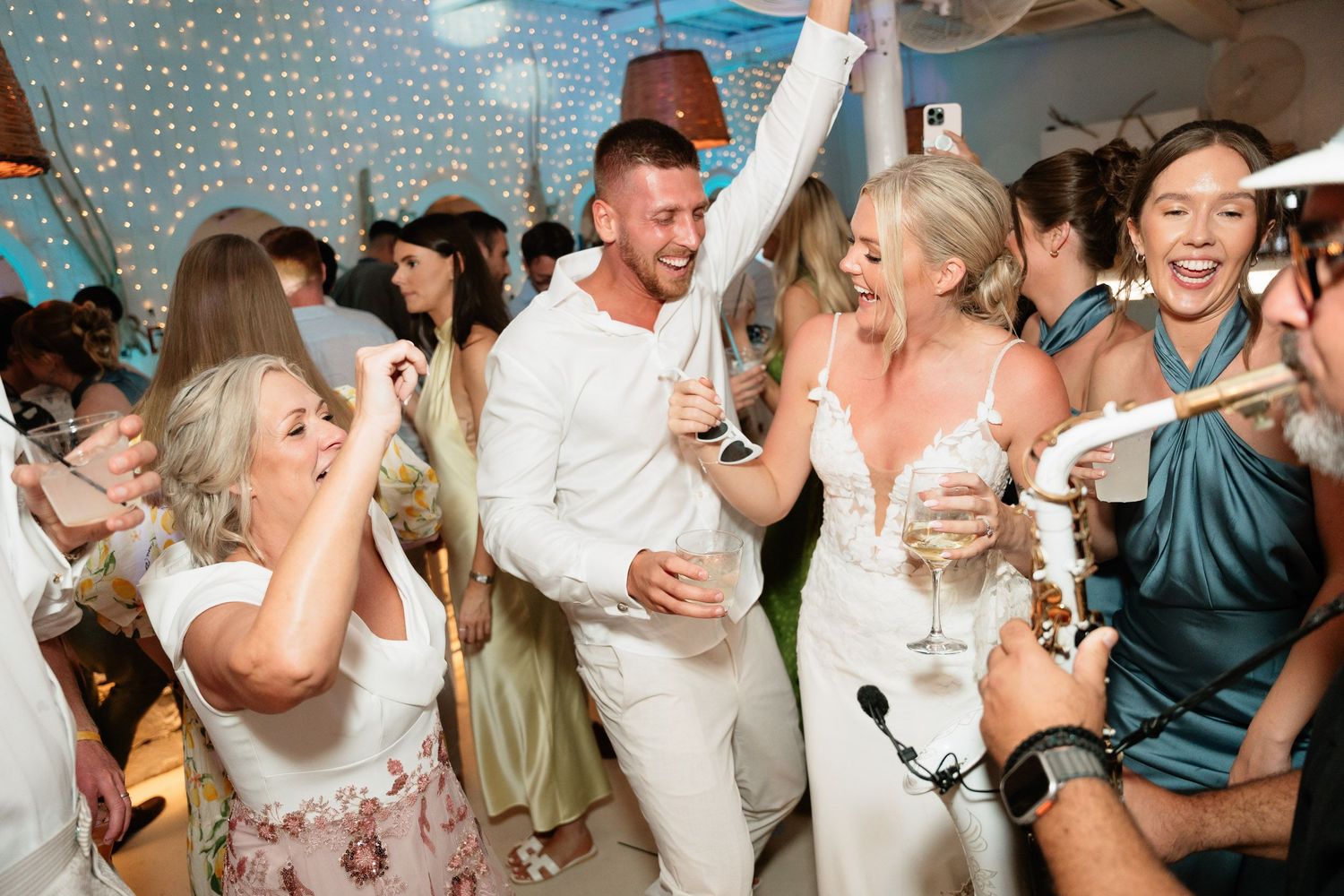Wedding guests dancing and celebrating together on a dance floor under twinkling lights at a reception party.